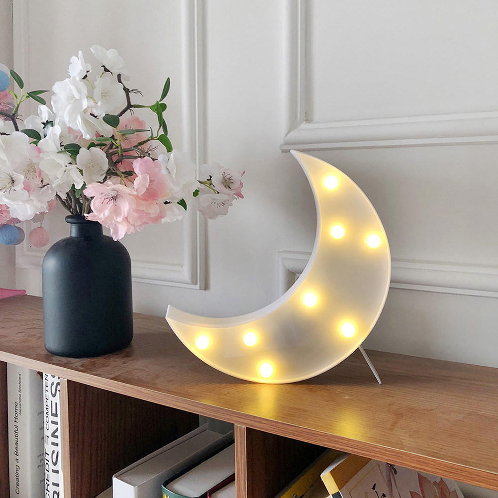 Eine dekorative Szene mit einem beleuchteten Mond, Blumen in einer Vase und Büchern auf einem Regal.