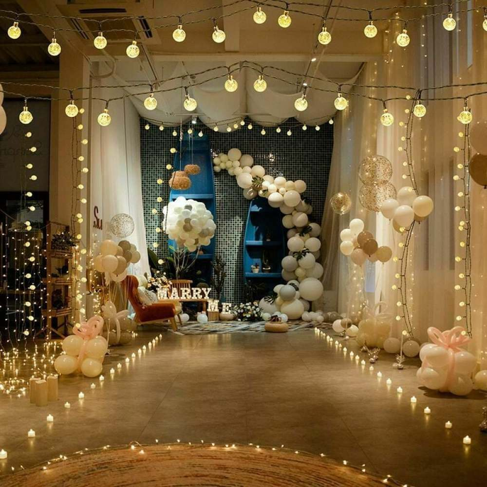 Ein dekorierter Raum mit Luftballons, Lichtern und einem 'Marry Me'-Schild. Kerzen und ein Stuhl schaffen eine romantische Atmosphäre.
