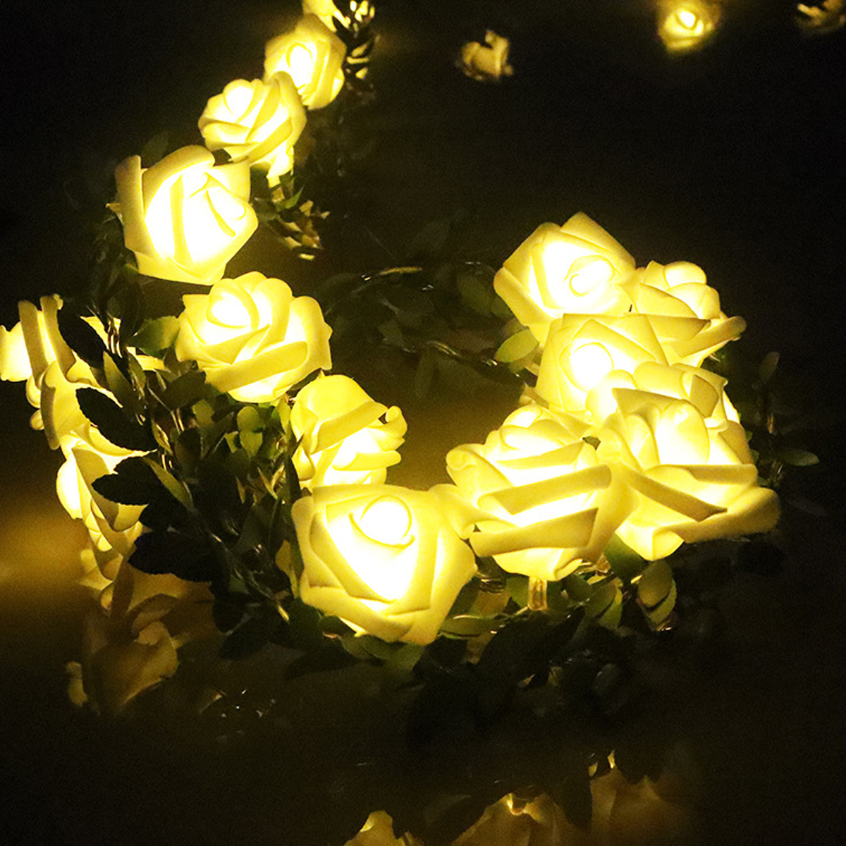 Eine Lichterkette aus gelb leuchtenden Rosen. Grüne Blätter und ein dunkler Hintergrund heben die beleuchteten Blumen hervor.