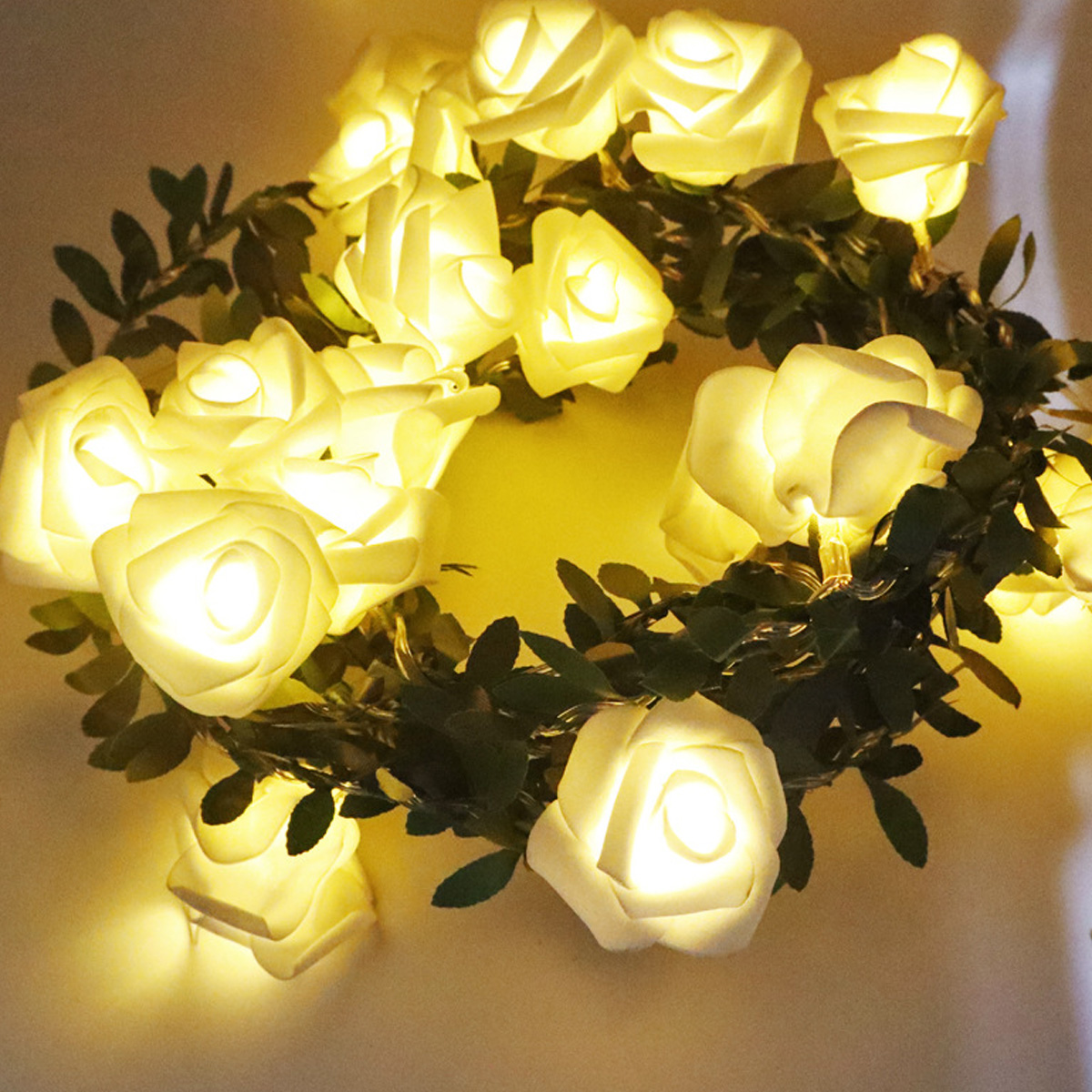 Eine kreisförmige Anordnung von beleuchteten weißen Rosenlichtern mit grünen Blättern. Die Lichter leuchten hell auf gelbem Hintergrund.