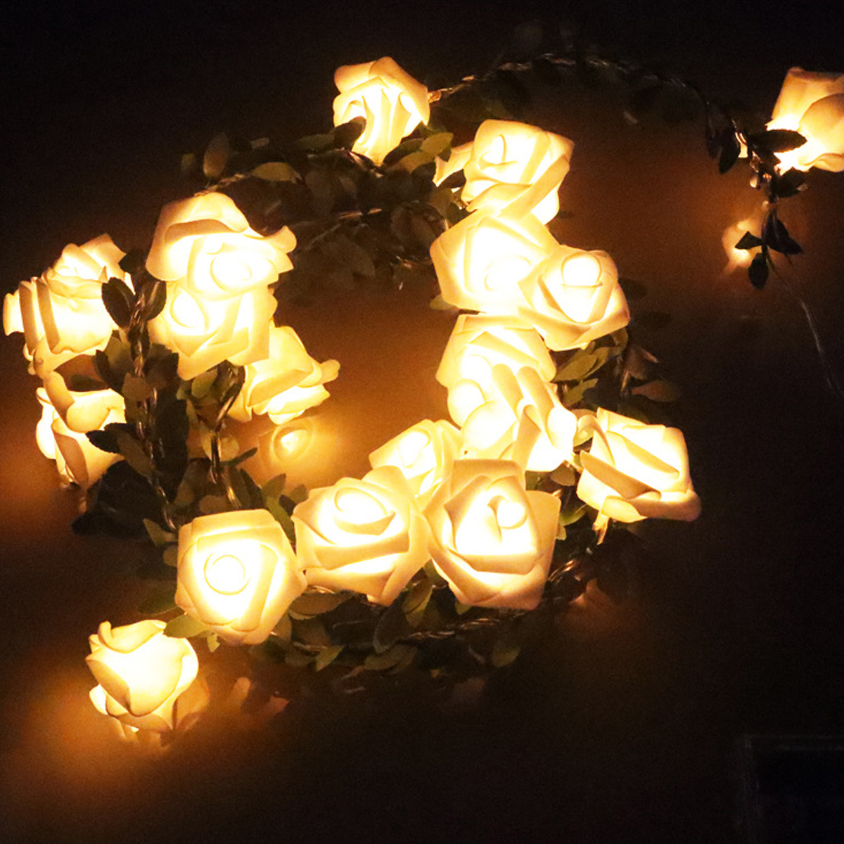 Eine Girlande aus leuchtenden, weißen rosenförmigen Lichtern. Grüne Blätter sind mit den Lichtern durchsetzt. Dunkler Hintergrund.