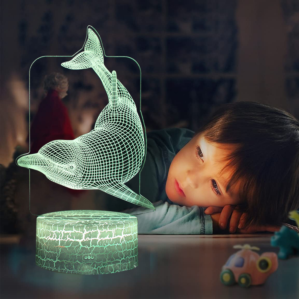 Ein Kind betrachtet eine delfinförmige Lampe. Die Lampe leuchtet grün und wirft ein weiches Licht. Spielzeug liegt in der Nähe verstreut.