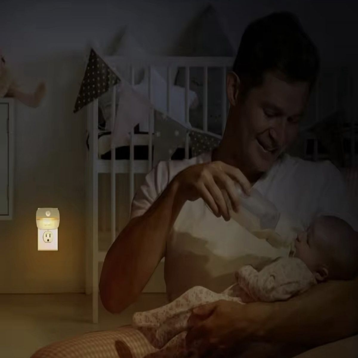 Ein Mann füttert ein Baby mit einer Flasche in einem dunklen Raum. Ein Nachtlicht ist an der Wand eingesteckt. Im Hintergrund ist ein Kinderbett.