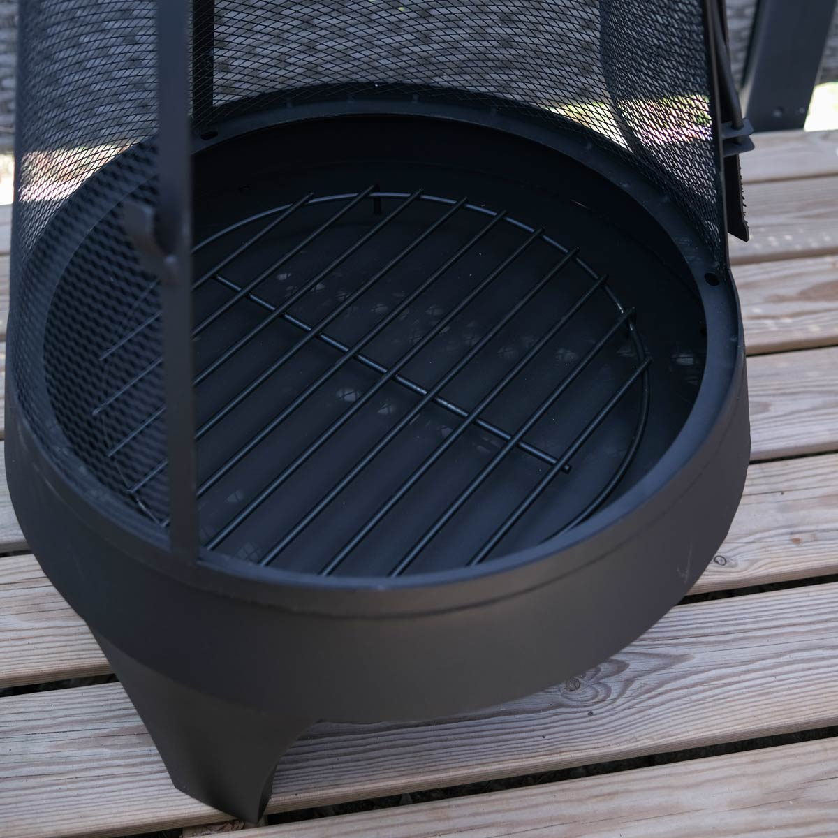 Nahaufnahme einer schwarzen Feuerstelle auf einer Holzterrasse. Sie hat einen Maschendraht, eine runde Basis mit Grill und eine Tür.