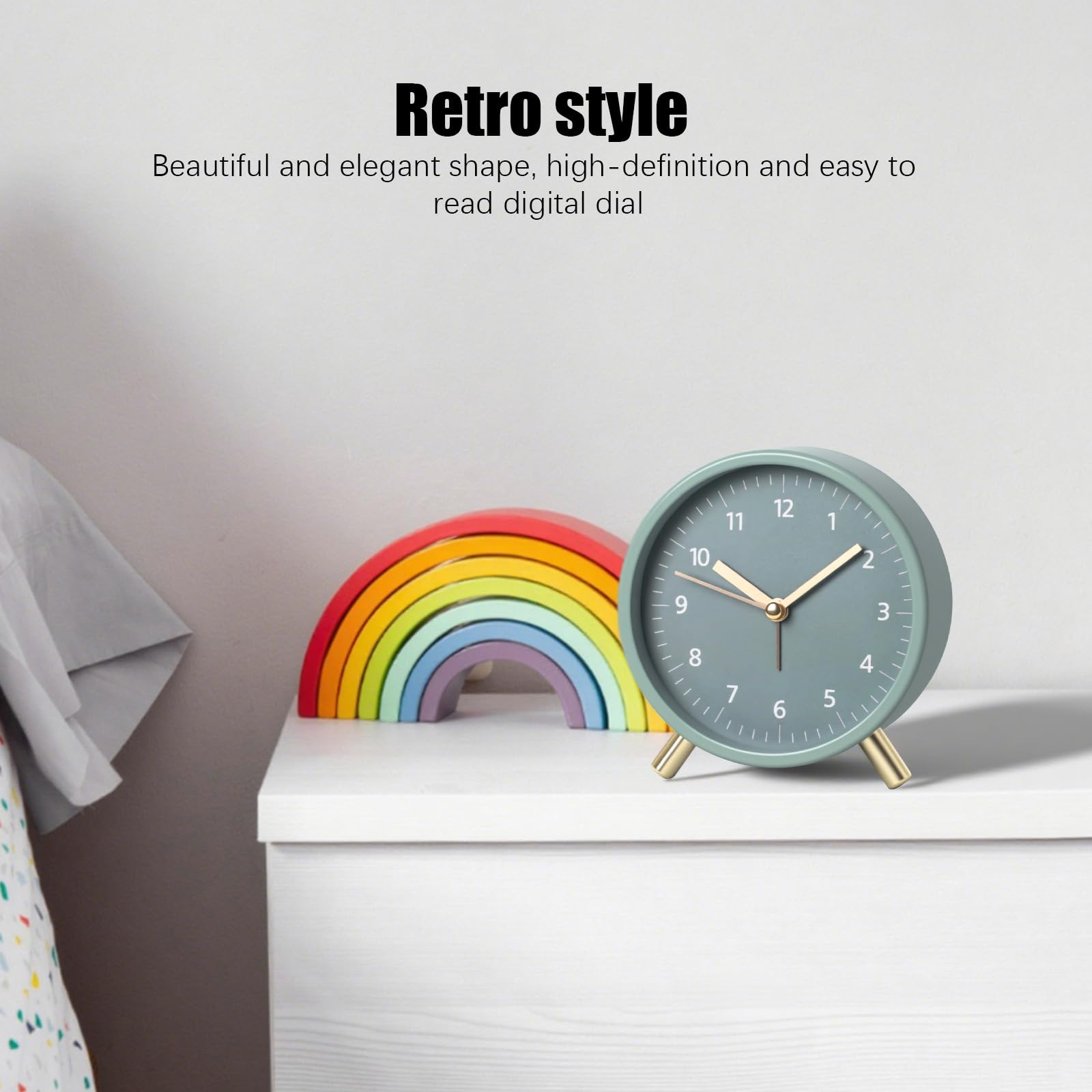 Eine mintgrüne Uhr mit goldenen Beinen steht auf einer weißen Oberfläche neben einem Holzregenbogen. Die Uhr zeigt die Zeit.
