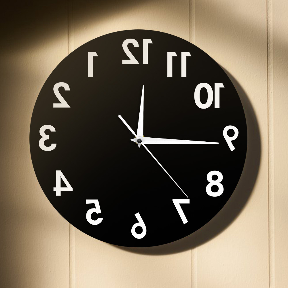 Eine schwarze Uhr mit weißen Zahlen und Zeigern. Die Zahlen sind gespiegelt. Sie hängt an einer beigefarbenen Wand. Es ist ungefähr 10:10 Uhr.