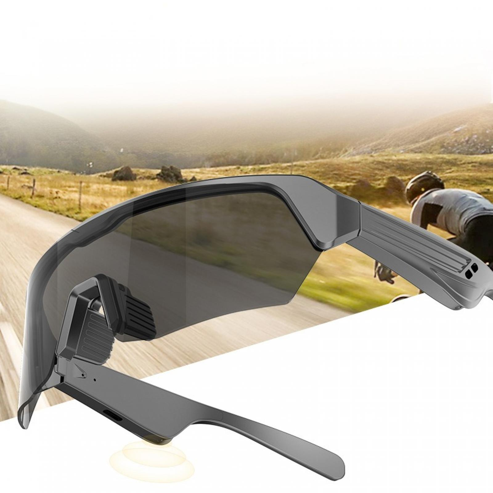 Sportsonnenbrille im Fokus, Radfahrer im Hintergrund. Sonnenbrille ist grau, Radfahrer trägt Helm und fährt auf Straße.