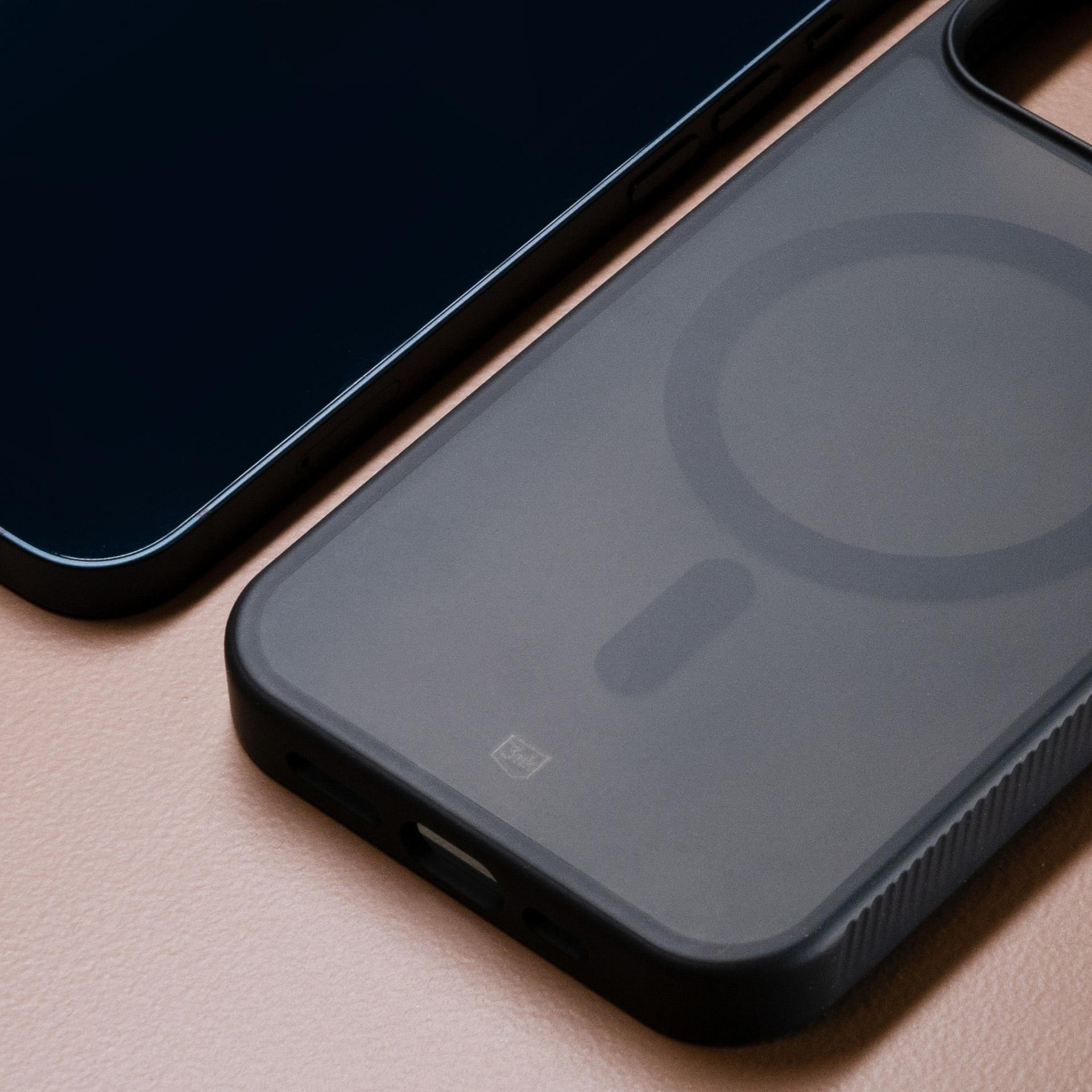 Telefono e custodia su superficie rosa. Il telefono è nero, la custodia grigia con design circolare.