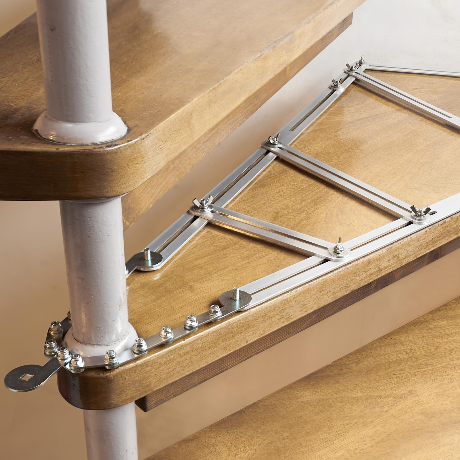Detail einer hölzernen Wendeltreppe mit silbernen Metallelementen. Die Stufen sind hellbraun, die Stütze weiß.