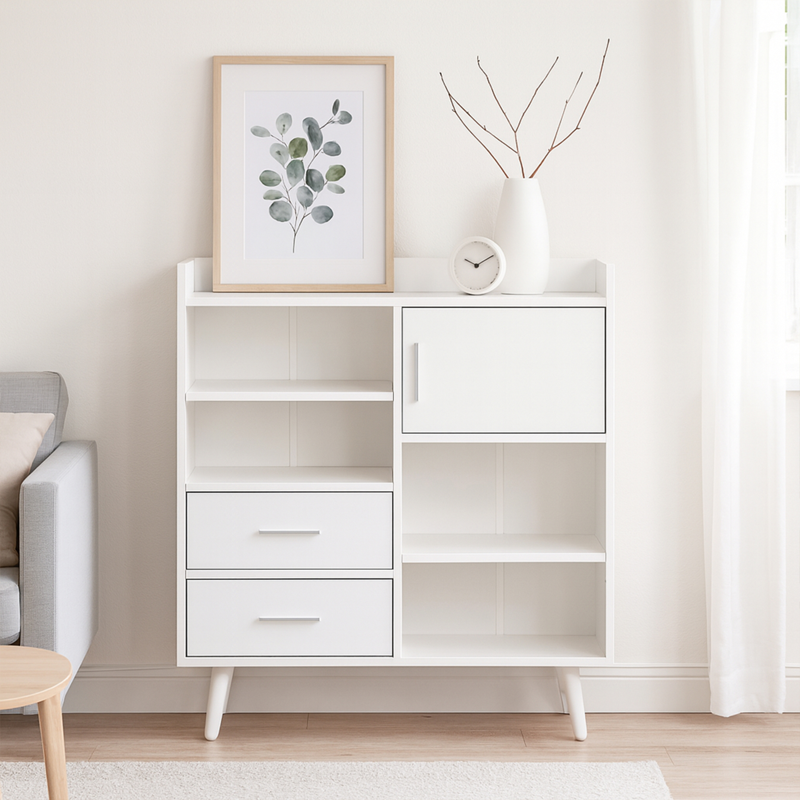 Weißer Schrank mit Schubladen, Bild und Uhr. Kahle Äste in Vase. Sofa und Holztisch sichtbar.