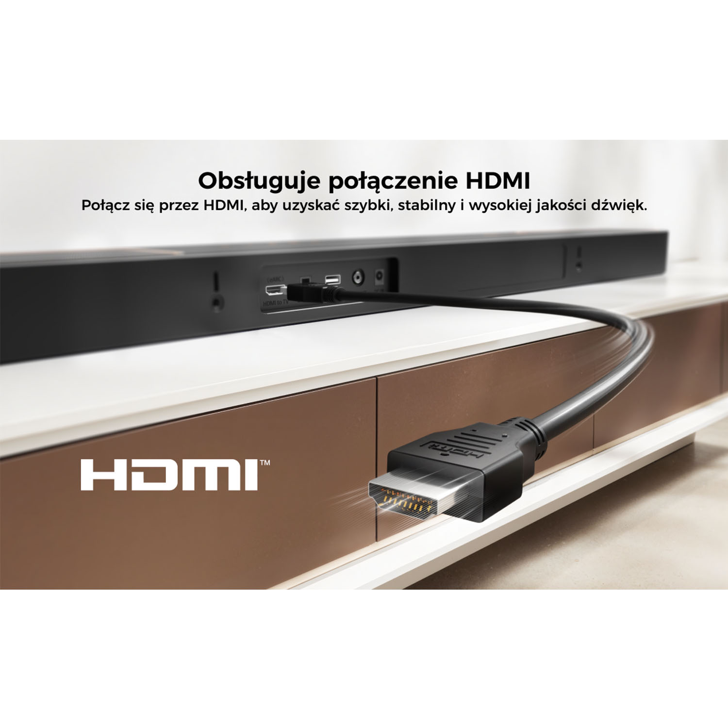 Kabel HDMI podłączony do soundbaru. Soundbar stoi na białej i brązowej szafce. Widoczne logo HDMI.