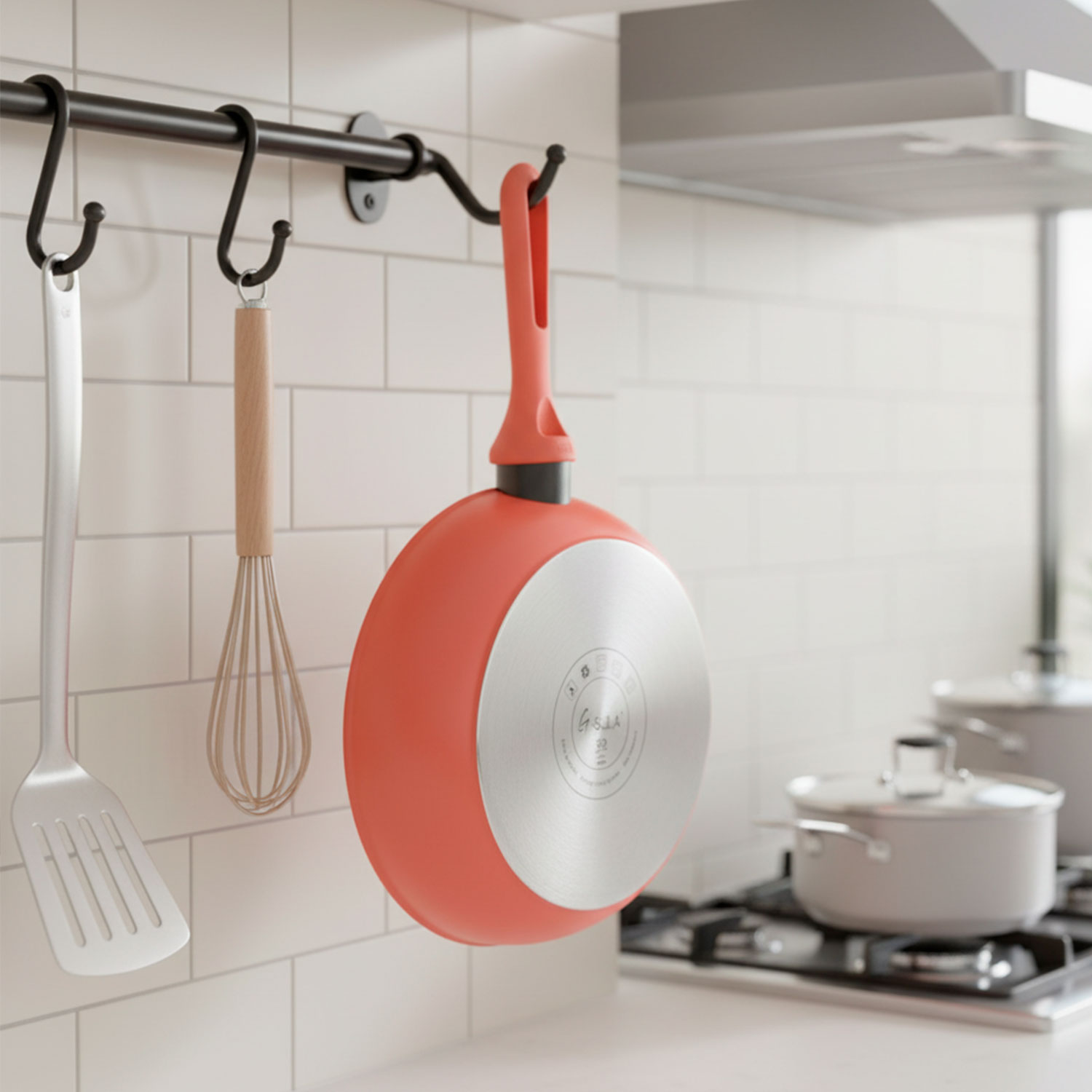 Escena de cocina con una sartén roja colgando de un riel con utensilios. Una espátula y un batidor cuelgan cerca. Otras ollas están en la estufa.