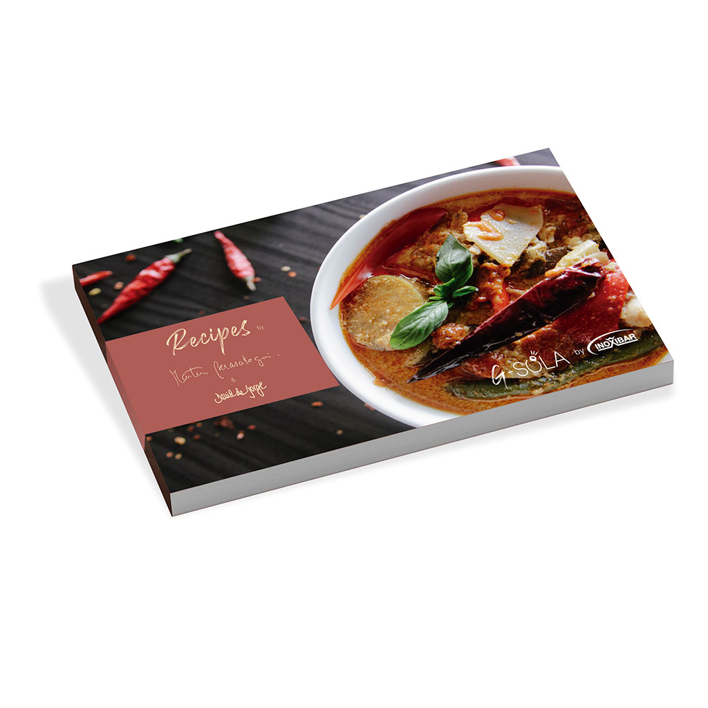 Un libro de cocina con un cuenco de curry. Chiles rojos esparcidos sobre una superficie oscura junto al libro. El libro se titula Recetas.