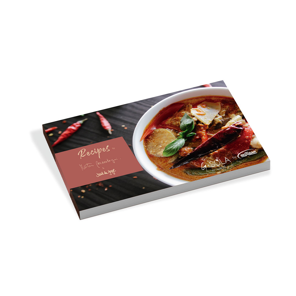 Un libro de cocina titulado 'Recetas' con un cuenco de curry. Chiles rojos sobre una superficie oscura. El libro está en ángulo.
