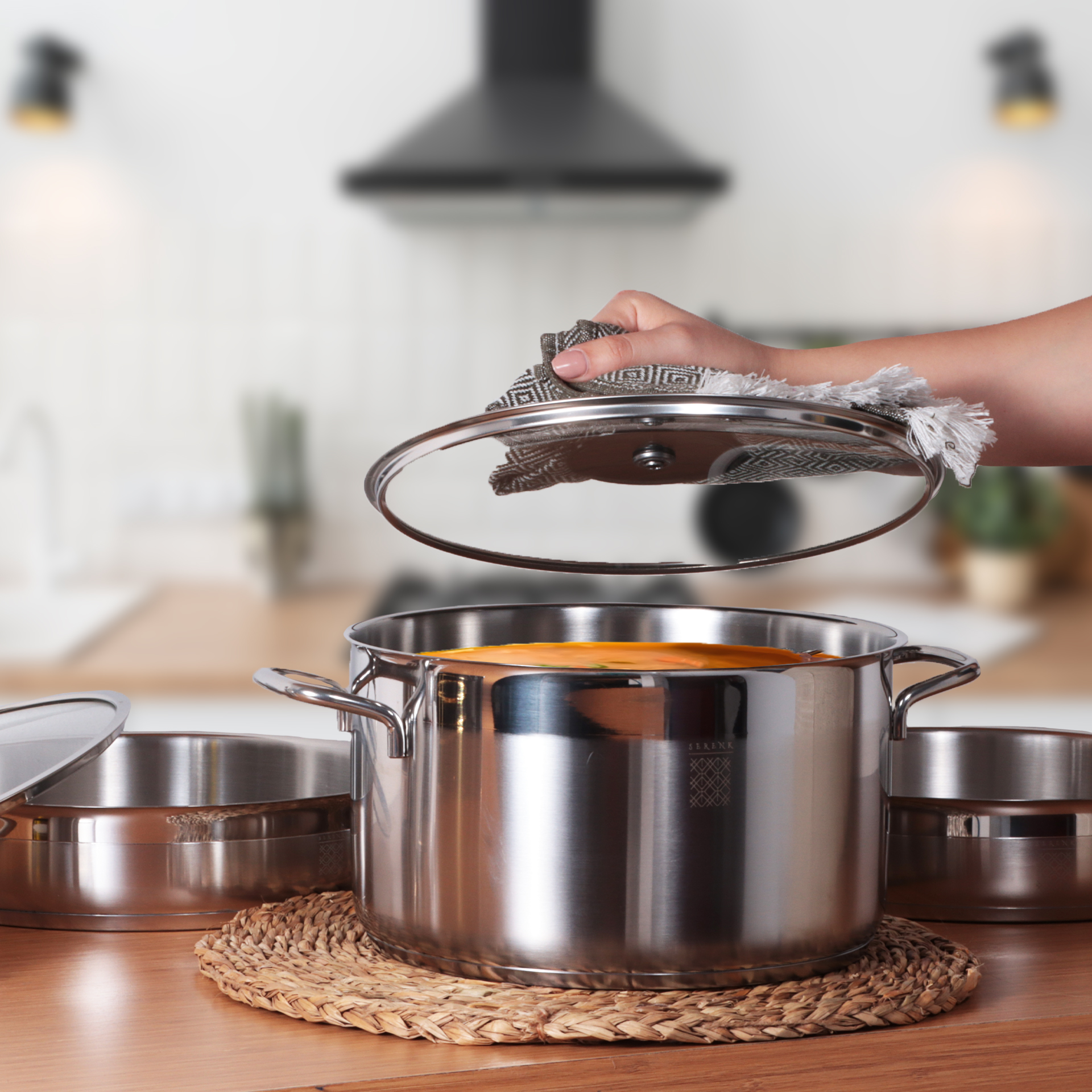 Una mano levanta la tapa de una olla. Una olla con líquido naranja sobre una mesa de madera.