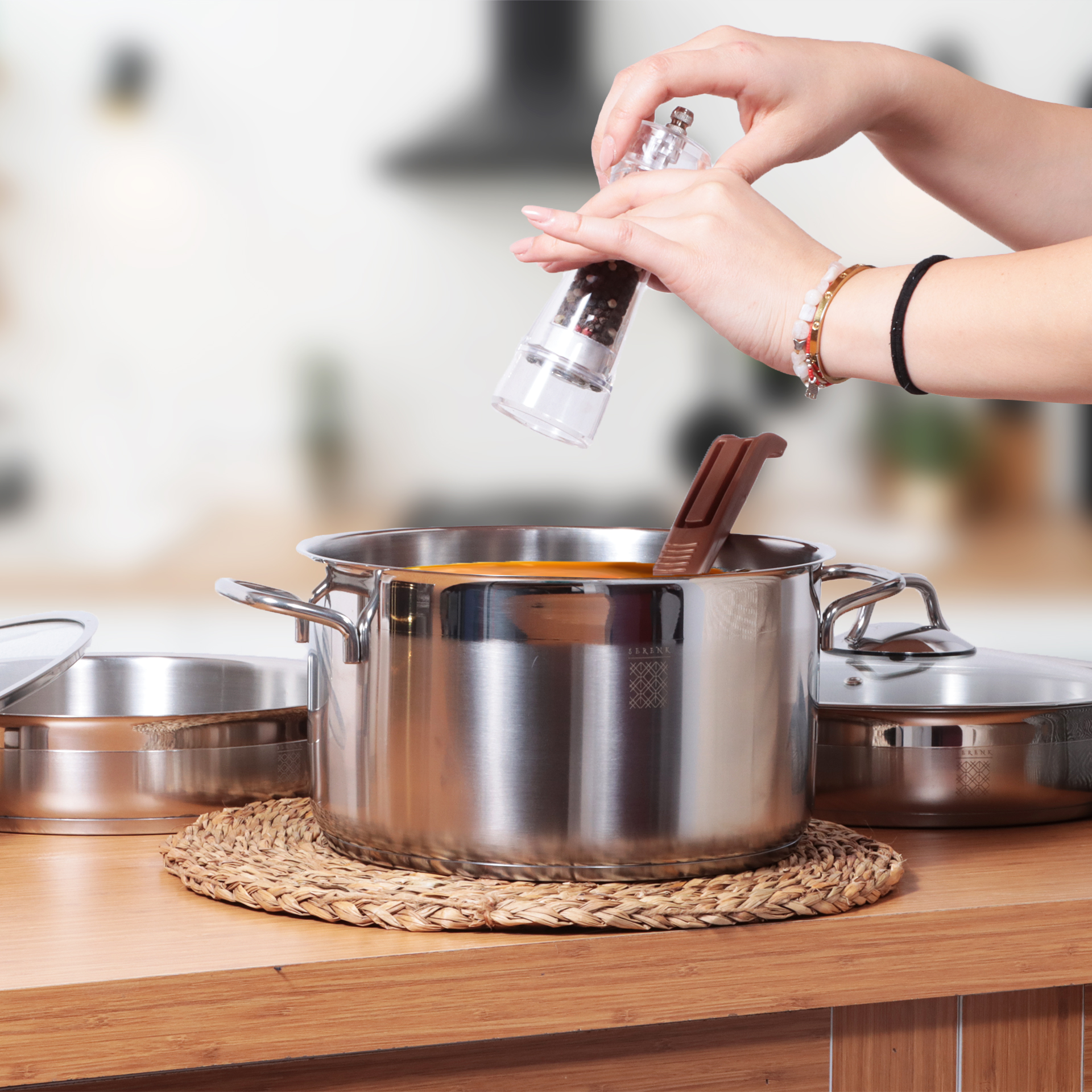 Manos moliendo pimienta en una olla de sopa. Ollas y tapas sobre una superficie de madera.