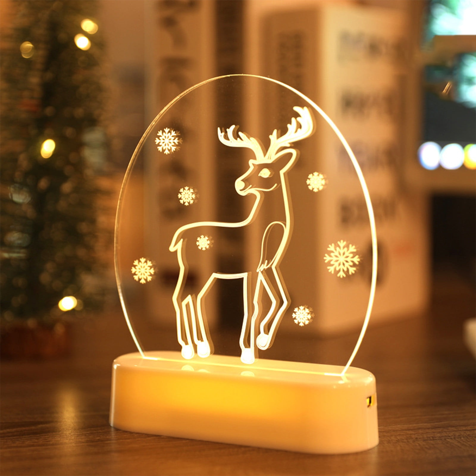 Ein leuchtendes Nachtlicht in Hirschform mit Schneeflocken. Es steht auf einem Ständer, mit einem verschwommenen Weihnachtsbaum im Hintergrund.