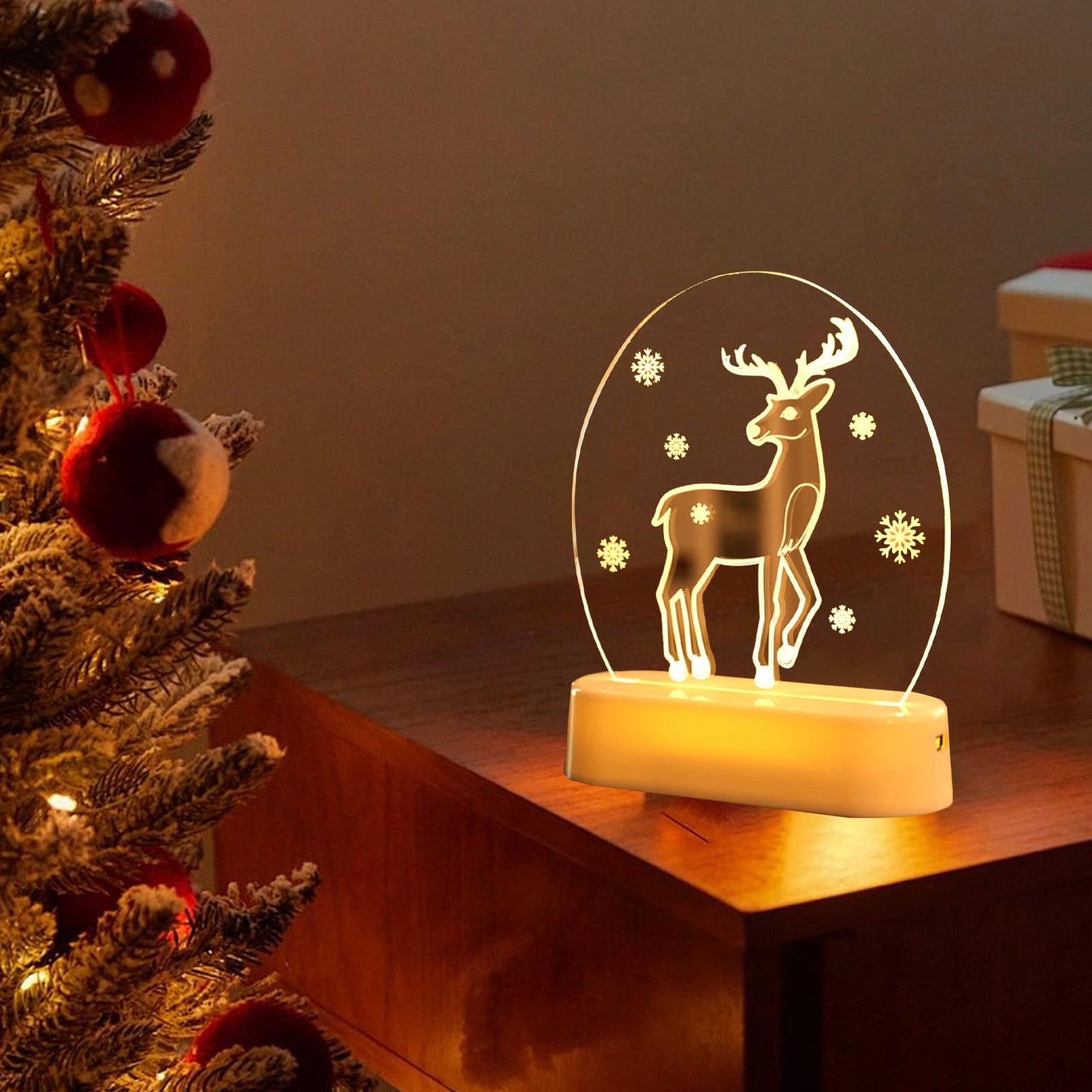 Eine leuchtende Rentierlampe mit Schneeflocken auf einem Holztisch, neben einem Weihnachtsbaum mit roten Ornamenten.