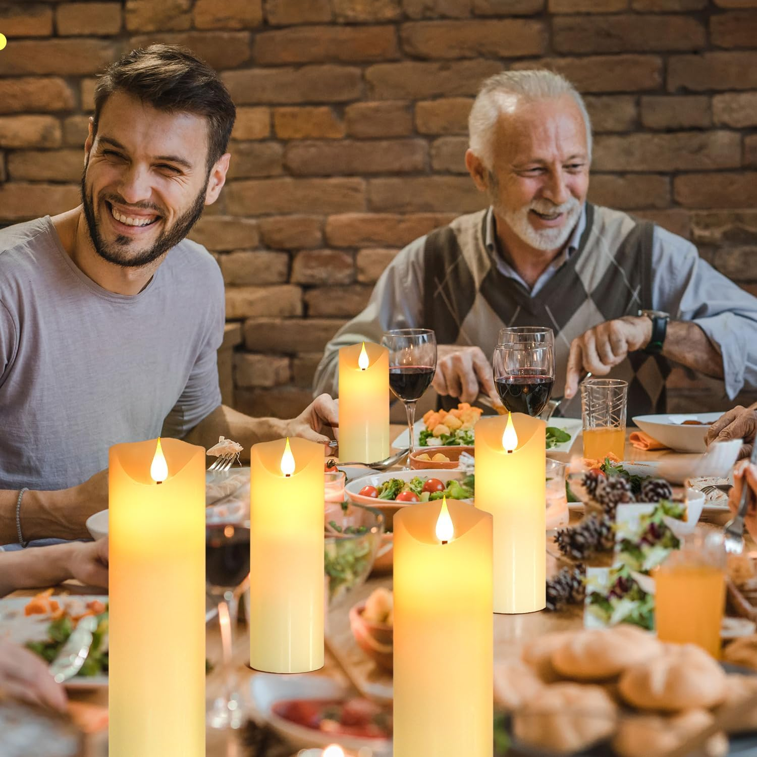 Eine Familie genießt ein Essen an einem Tisch mit brennenden Kerzen. Lachende Männer sitzen, Essen und Getränke stehen auf dem Tisch. Eine Backsteinmauer ist der Hintergrund.
