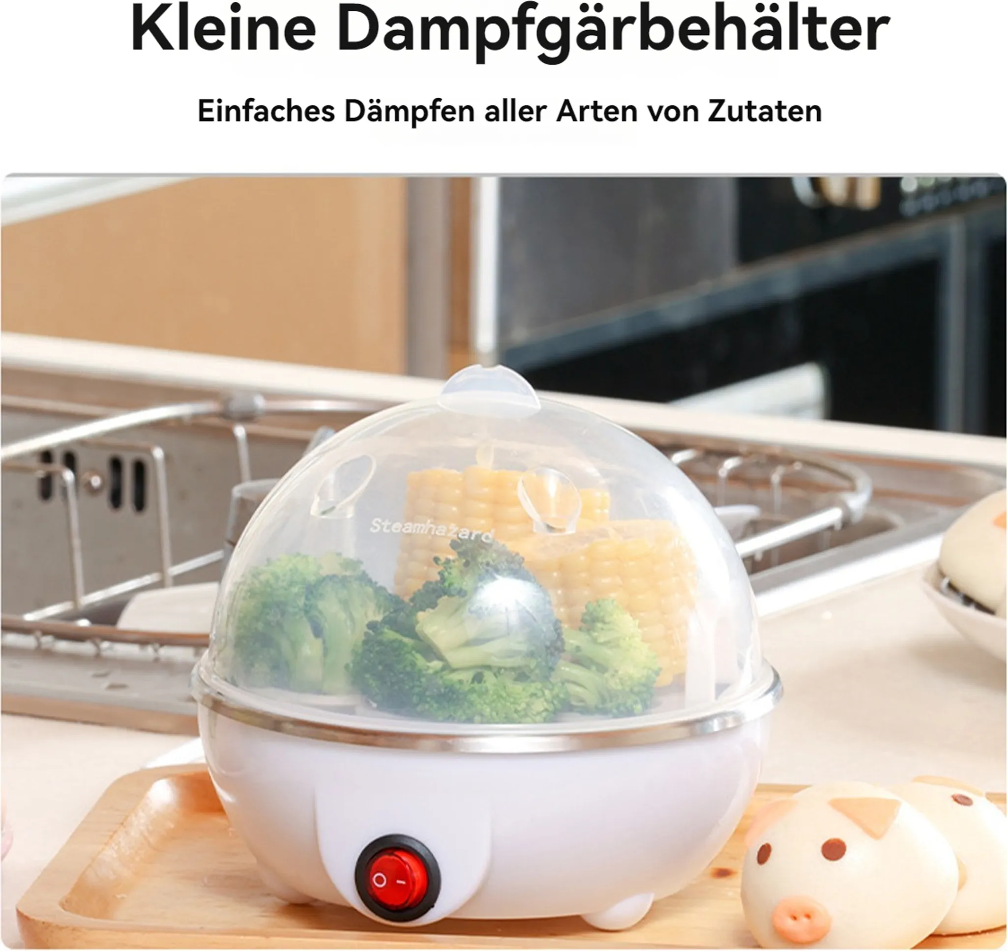 Ein weißer Dampfgarer mit Brokkoli und Mais darin. Vorne ist ein roter Schalter. Schweineförmige Brötchen im Hintergrund.
