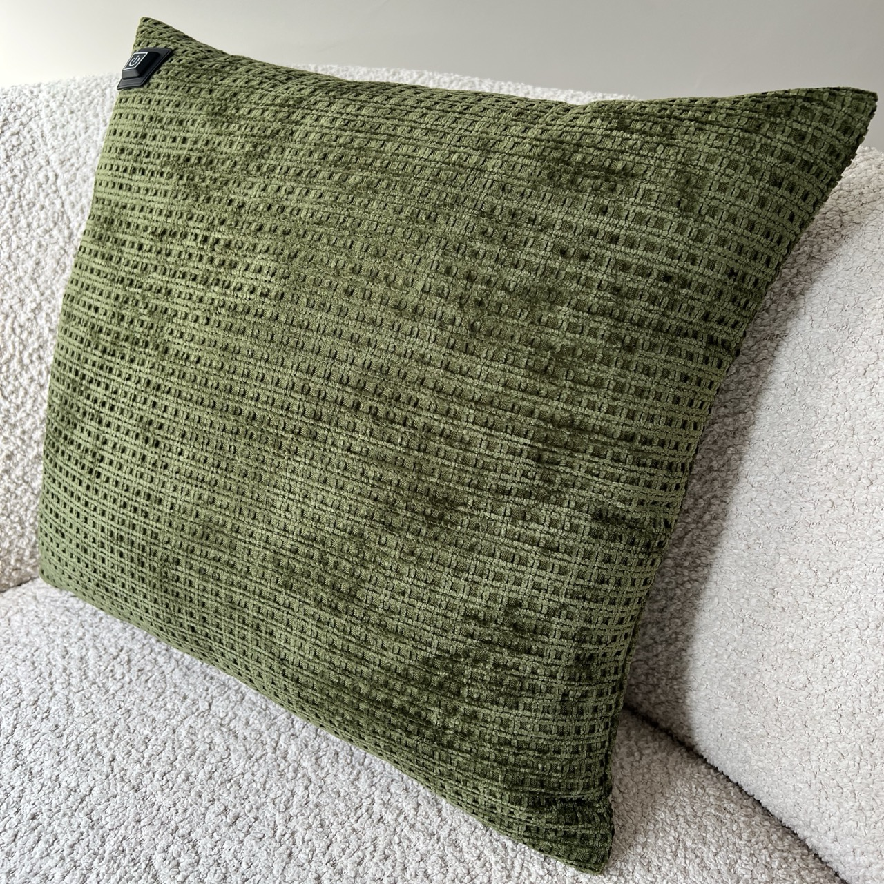 Ein olivgrünes, strukturiertes Kissen liegt auf einem cremefarbenen, strukturierten Sofa. Das Kissen hat ein quadratisches Muster.