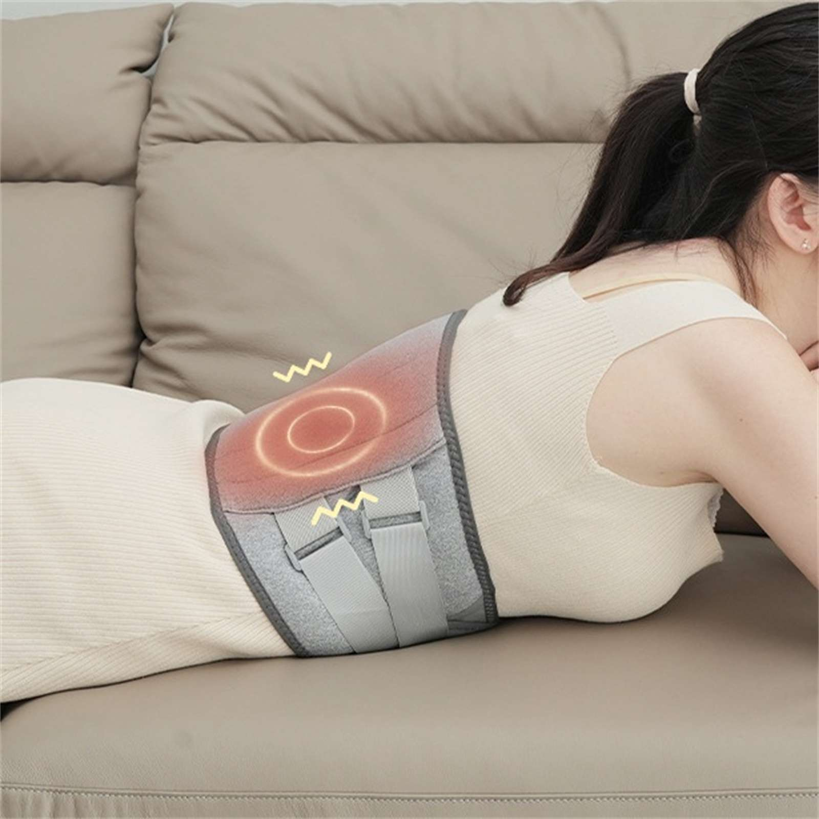 Frau liegt auf einer Couch mit Rückenstütze. Die Orthese hat ein rotes Wärmesymbol. Beige Couch und Kleid der Frau.