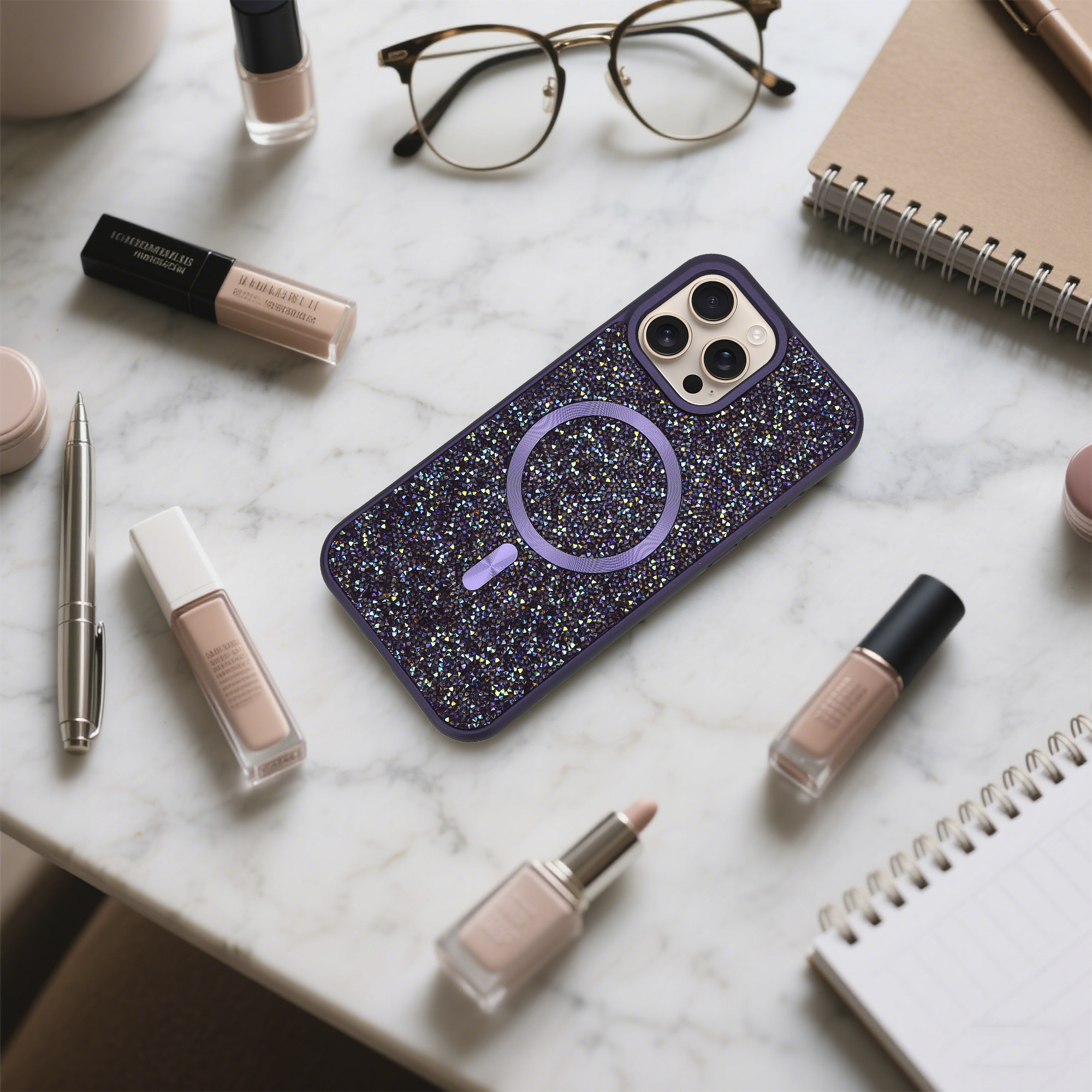 Auf einer Marmoroberfläche befinden sich eine Handyhülle, Make-up, eine Brille und ein Notizbuch. Die Handyhülle ist lila und mit Glitzer bedeckt.