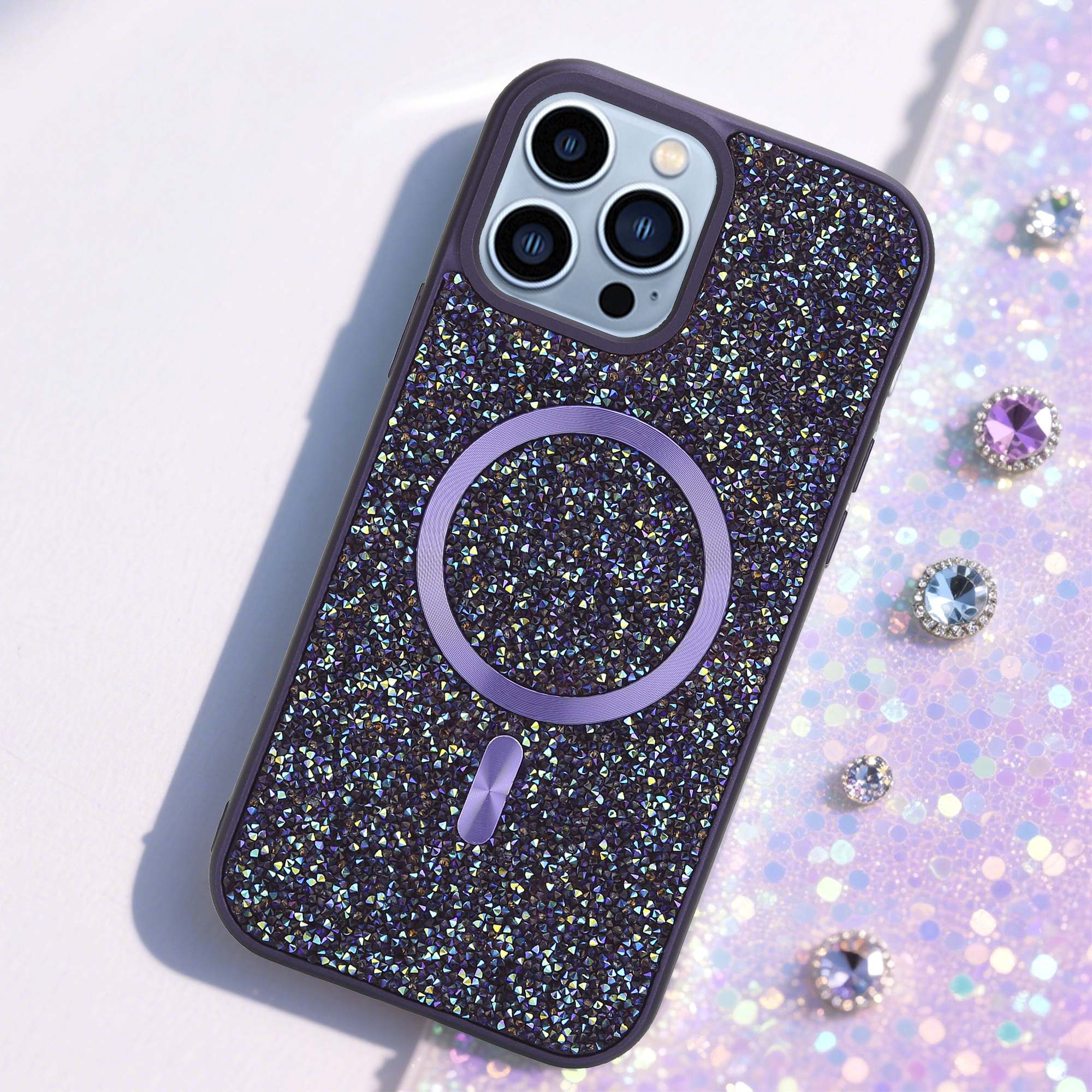 Ein mit Strass besetztes Handycase mit lila Ring und Edelsteinen auf glitzerndem Hintergrund.