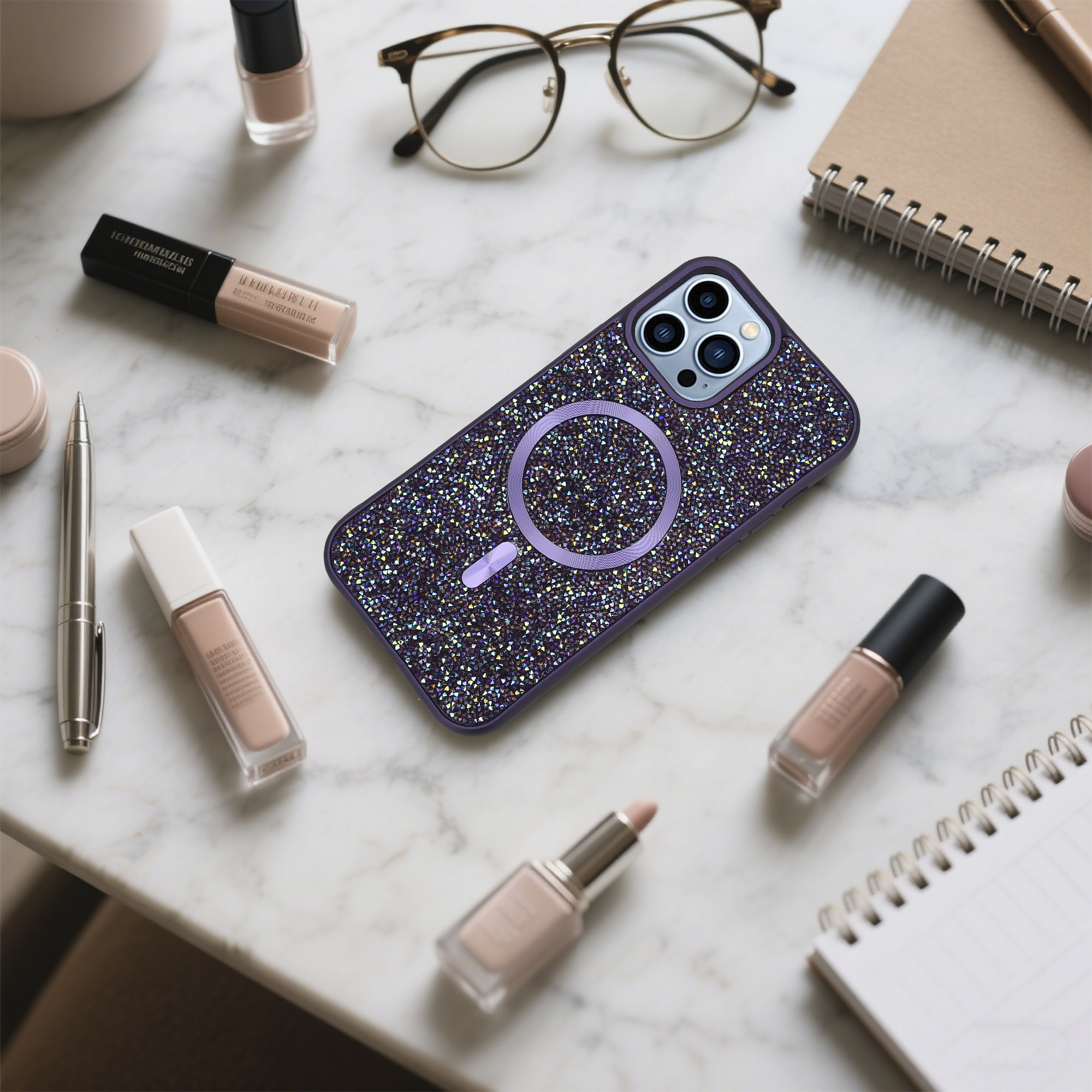 Eine Handytasche mit Kristallen, Brille, Make-up und ein Notizblock liegen auf einer Marmoroberfläche.