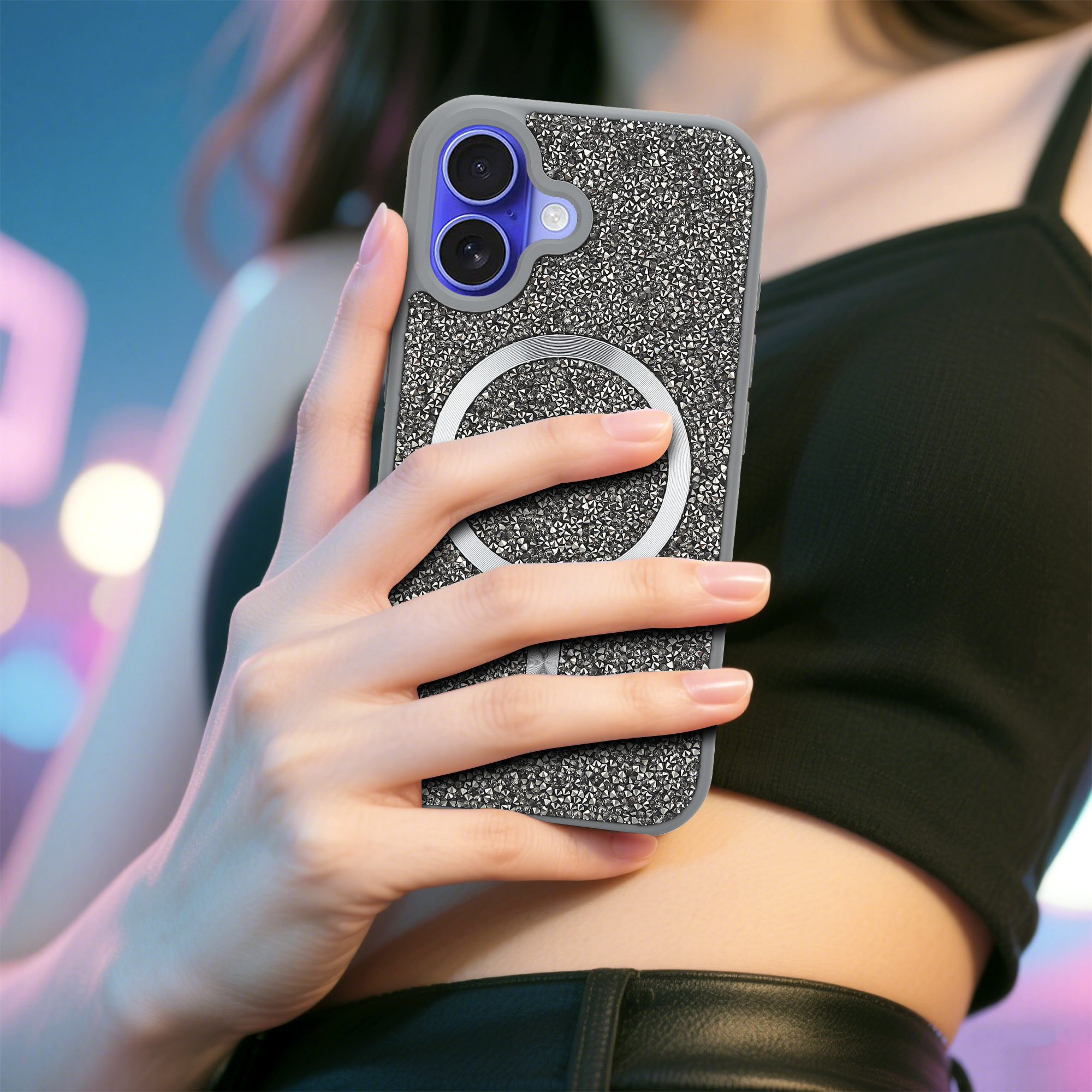 Eine Frau hält ein Telefon mit einer glitzernden Hülle. Der Hintergrund ist ein verschwommener Farbmix mit schwarzem Oberteil und Lederhose.