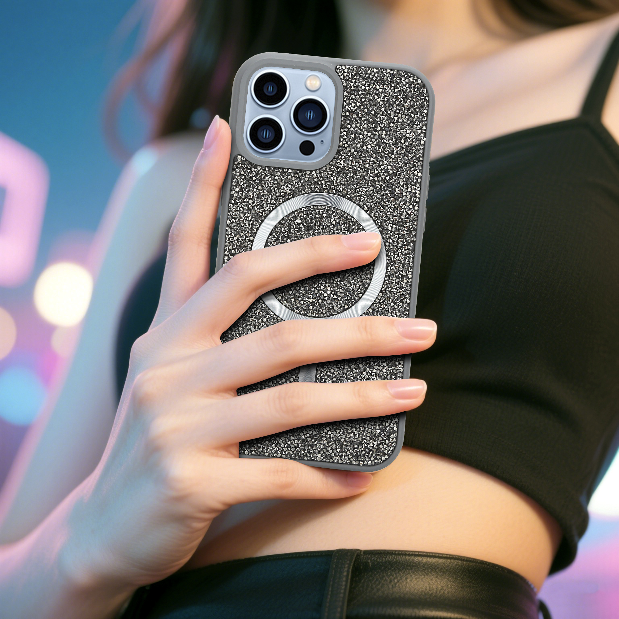 Eine Frau hält ein Handy mit einer glitzernden Hülle. Das Telefon ist silber und schwarz, mit einem MagSafe-Ring.