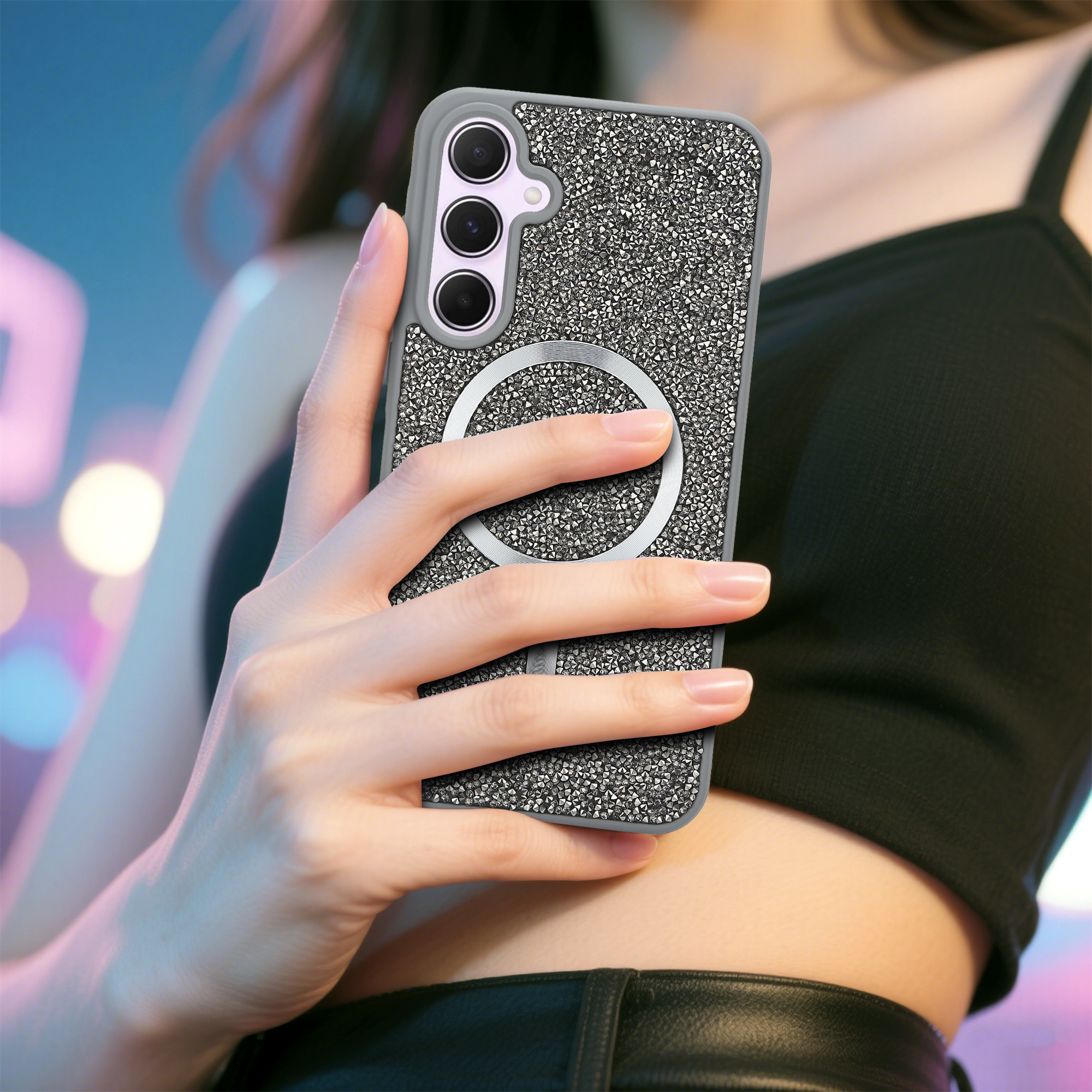Eine Frau hält ein Handy in einer glitzernden Hülle. Das Telefon hat einen silbernen Ring auf der Rückseite. Sie trägt ein schwarzes Oberteil.