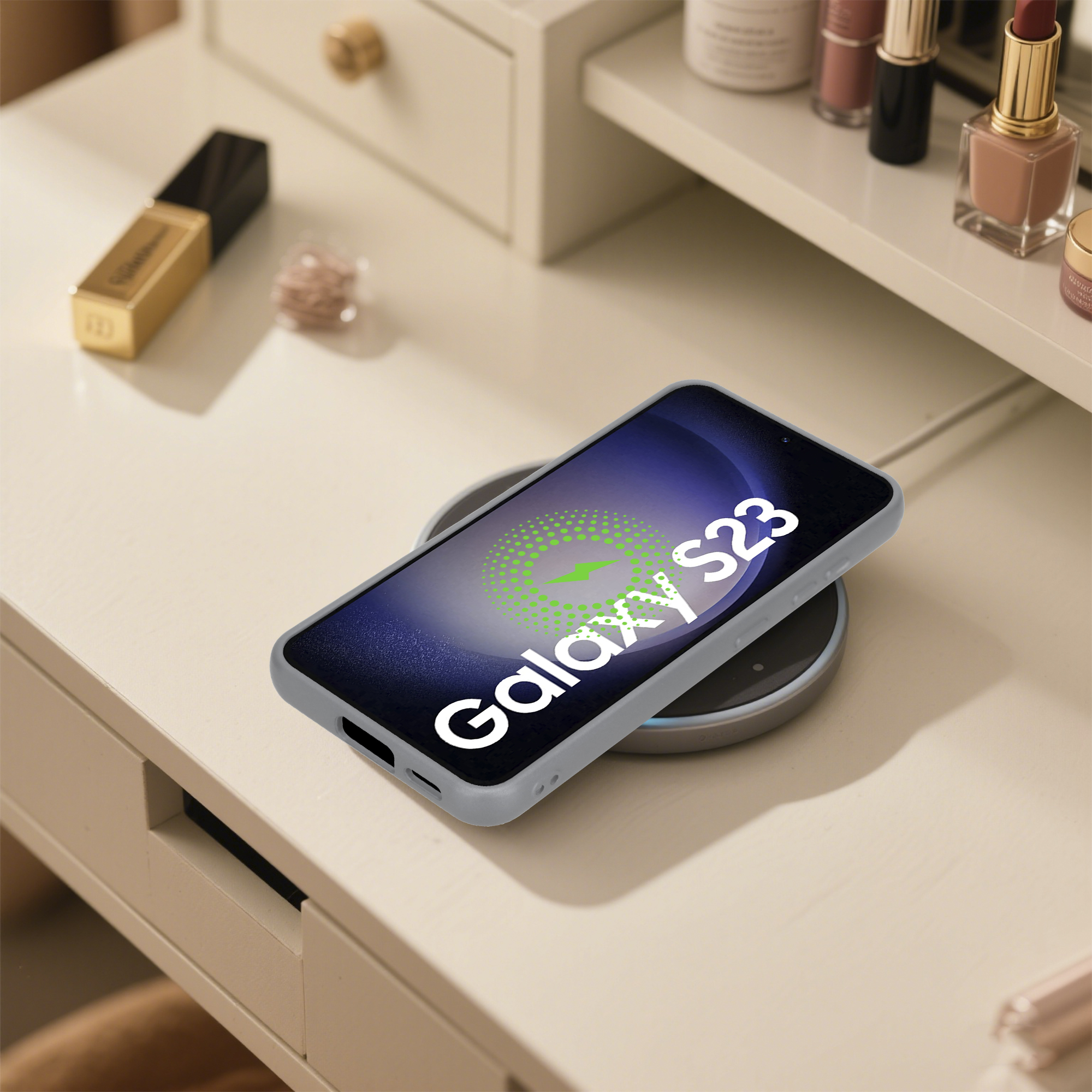 Ein Galaxy S23-Telefon, das drahtlos auf einem Schreibtisch aufgeladen wird. Lippenstift und andere Make-up-Artikel sind im Hintergrund.