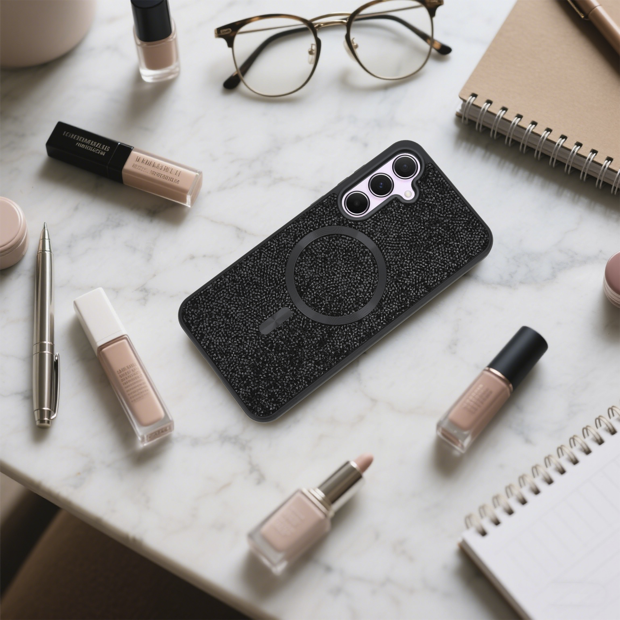 Eine Handyhülle, Make-up, eine Brille und ein Notizbuch sind auf einer Marmoroberfläche angeordnet.