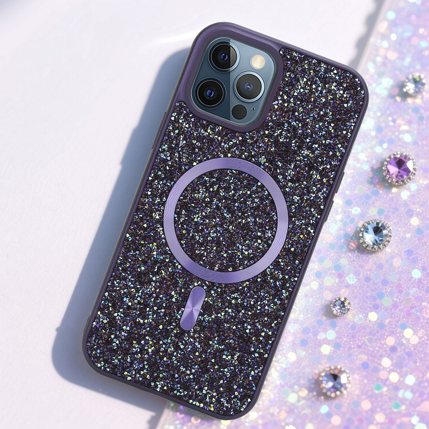 Lila Handyhülle mit glitzernden Kristallen und kreisförmigem Ladegerät. Mehrere Juwelen sind darum verstreut.