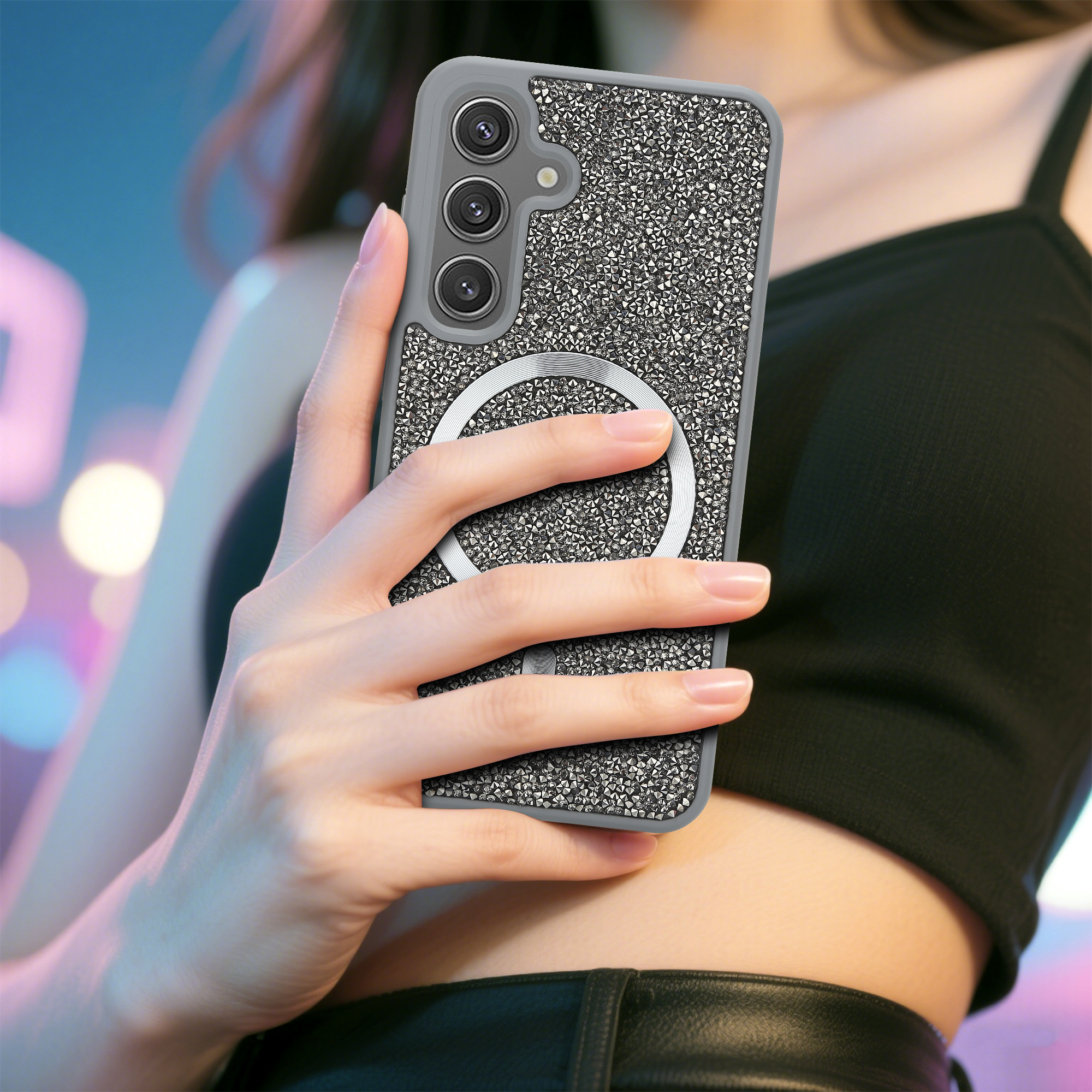 Eine Frau hält ein Handy in einer glitzernden Hülle. Die Hülle hat einen Magnetring. Der Hintergrund ist mit blauen und rosa Lichtern verschwommen.