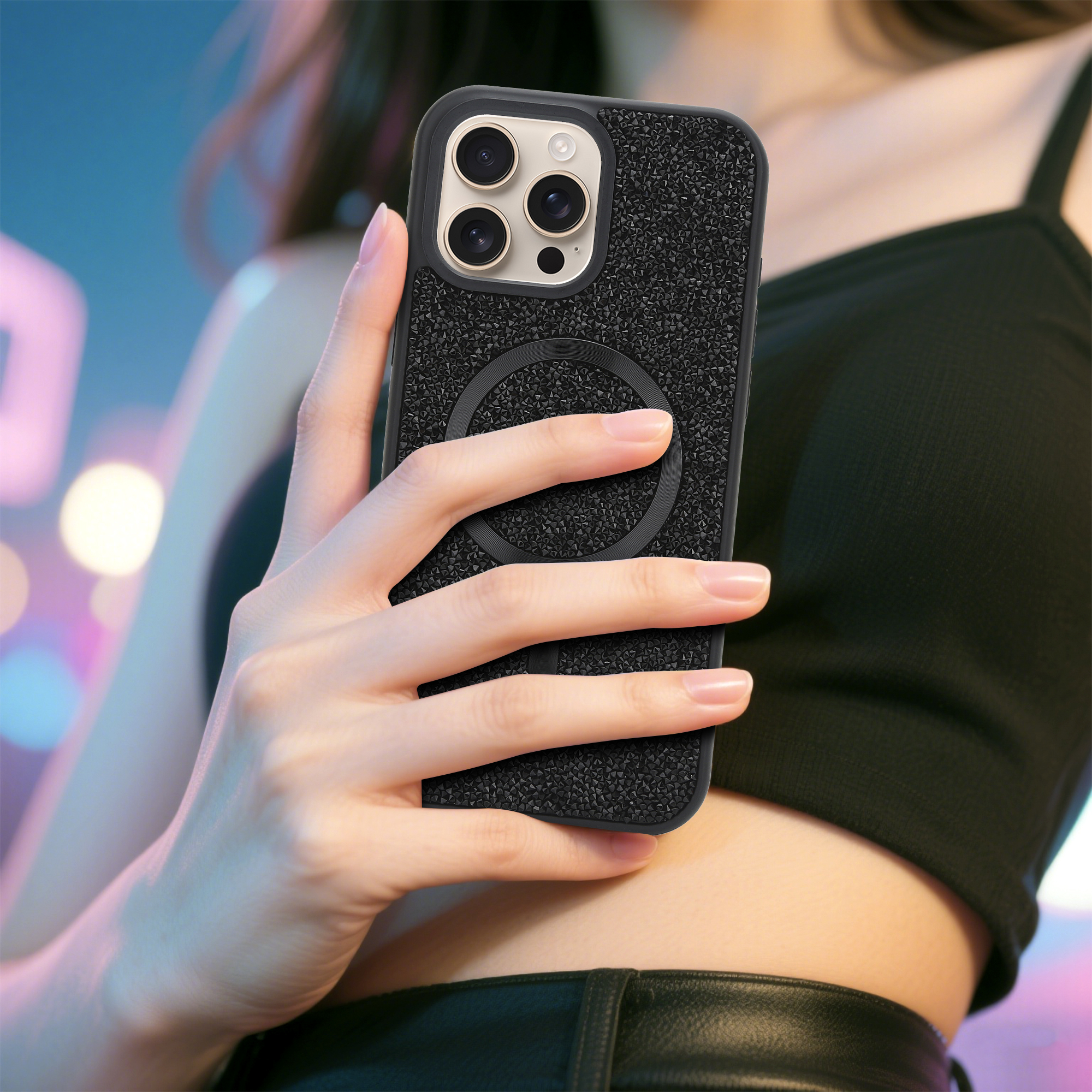 Eine Person hält ein schwarzes Telefon mit Hülle. Das Telefon hat drei Kameralinsen. Der Hintergrund ist mit blauen und rosa Lichtern verschwommen.