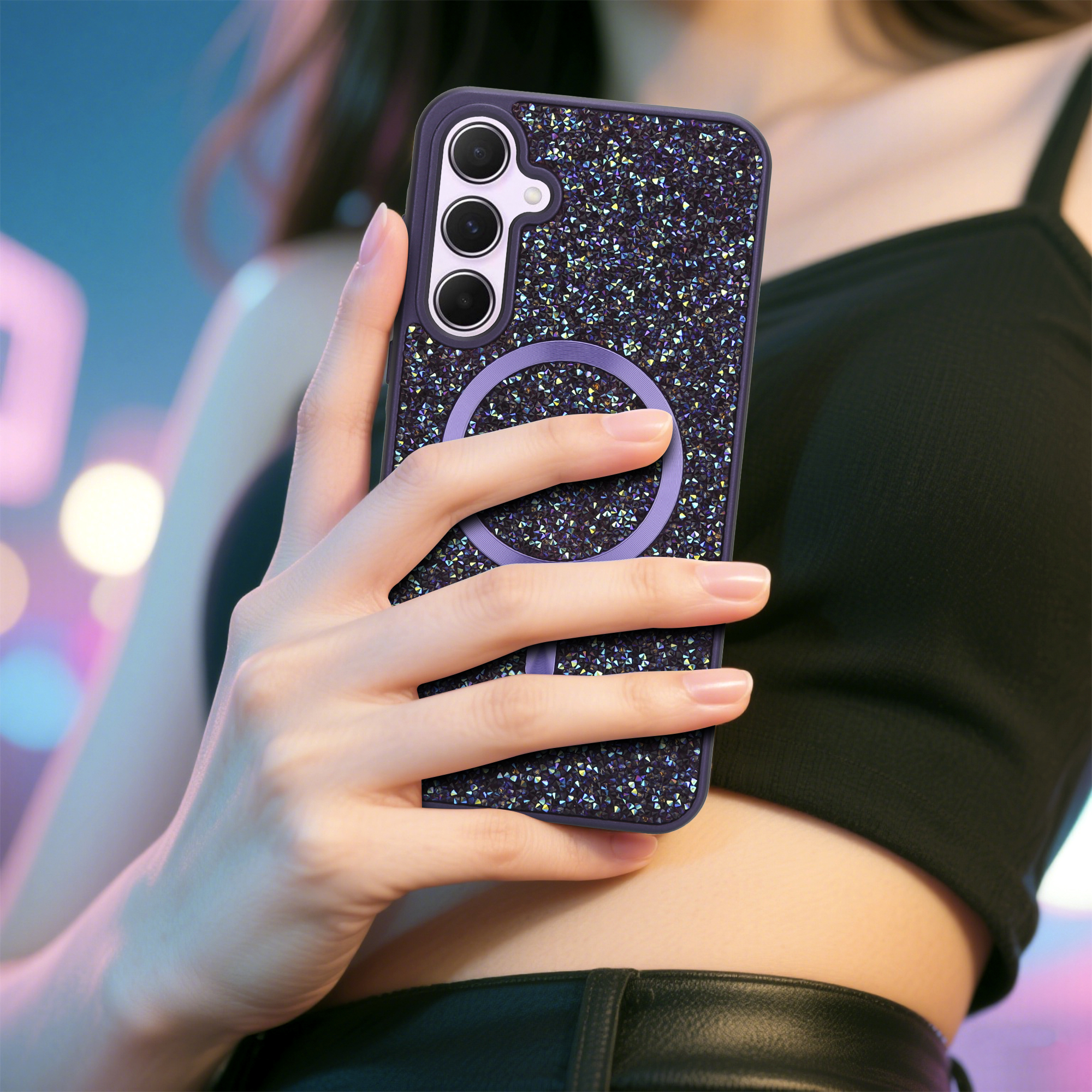 Eine Hand hält ein Telefon mit einer glitzernden Hülle. Der Hintergrund ist verschwommen, eine Person in einem schwarzen Top.