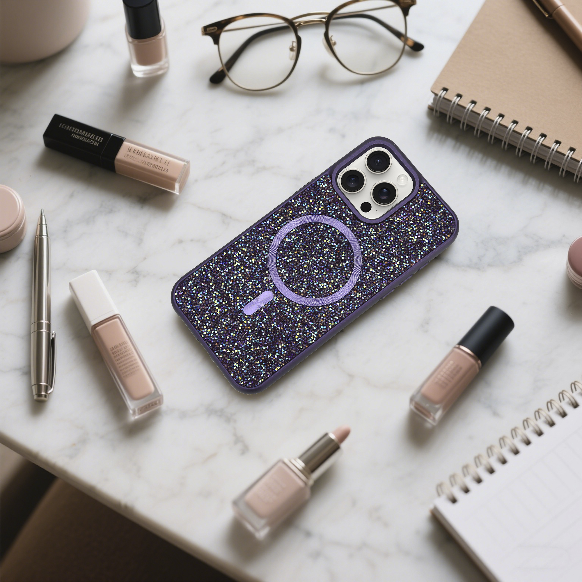 Lila Handyhülle mit Kristallen, Brille, Make-up, Nagellack, Stift und Notizbuch auf Marmor.