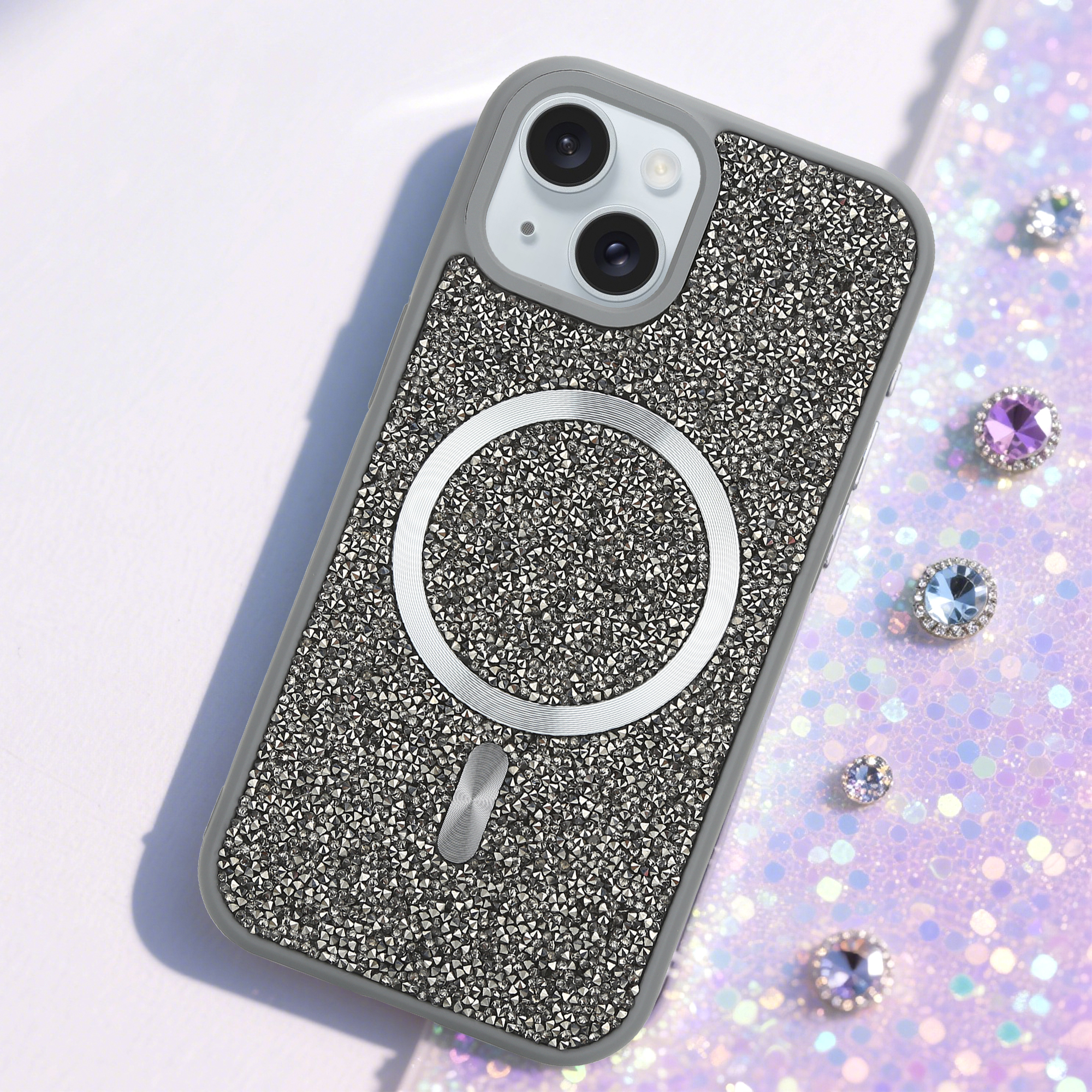 Eine mit Kristallen besetzte Handyhülle auf einem glitzernden lila Hintergrund mit verstreuten Juwelen.