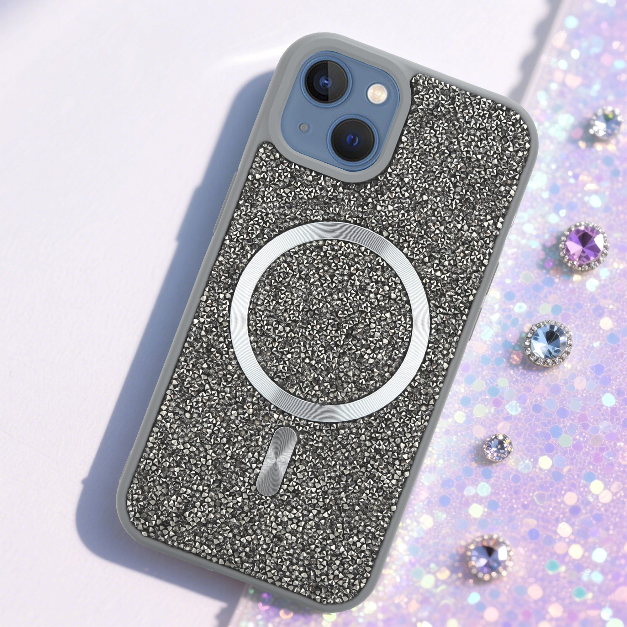 Ein iPhone-Case mit Kristallverzierungen. Ein silberner Ring und ein kleines silbernes Rechteck befinden sich auf der Rückseite. Edelsteine sind verstreut.