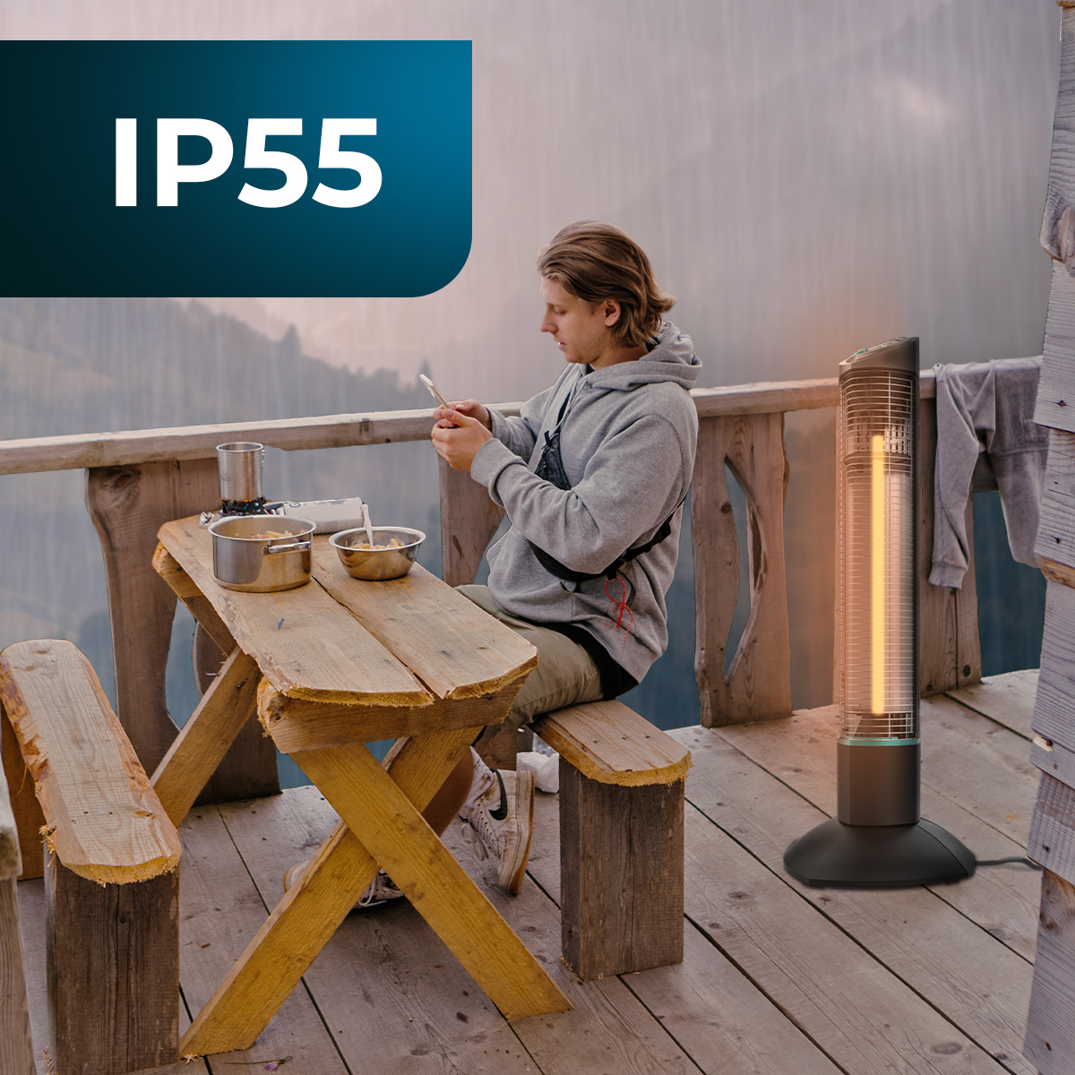 Mężczyzna używa telefonu przy stole z jedzeniem. Grzejnik jest w pobliżu. W tle widok na góry.