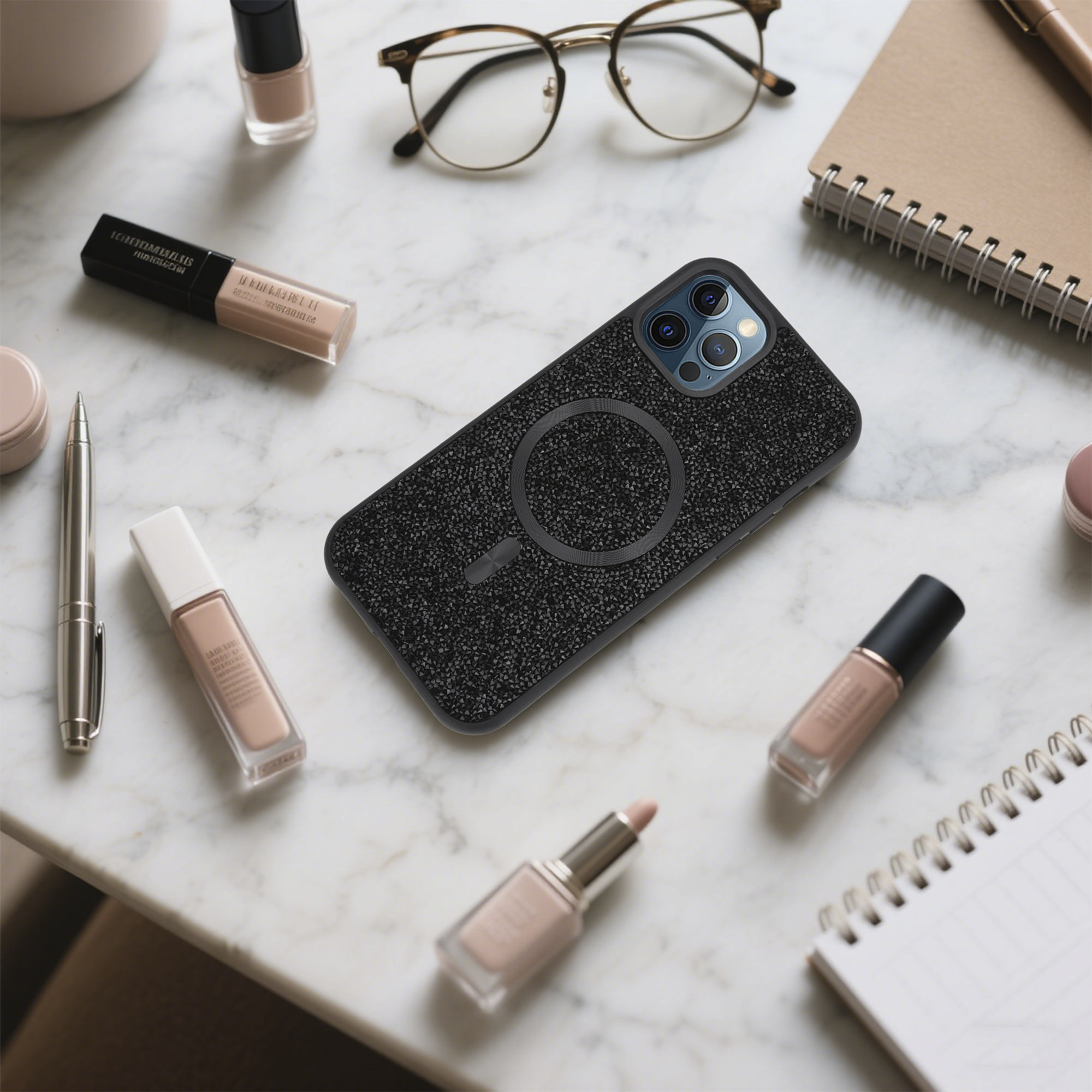 Ein Telefon in einer strukturierten Hülle liegt auf einer Marmoroberfläche, umgeben von Make-up, Brille und Notizbuch.
