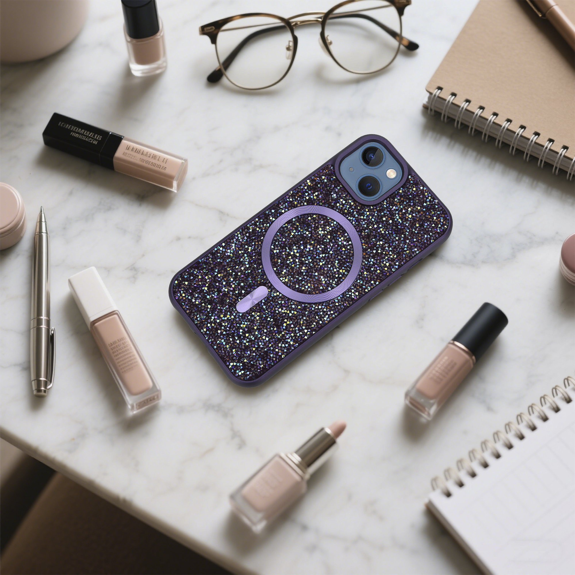 Eine Handytasche mit Kristallen, Make-up, Brille und Notizblock liegen auf einer Marmoroberfläche.