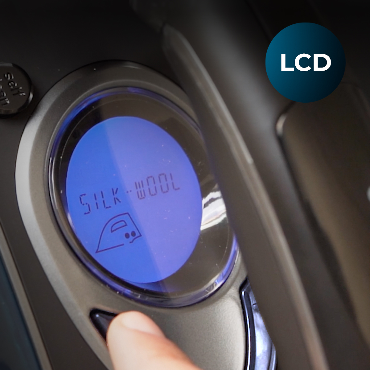 Zbliżenie panelu sterowania żelazka. Ekran LCD wyświetla 'SILK-WOOL'. Palec naciska przycisk poniżej ekranu.