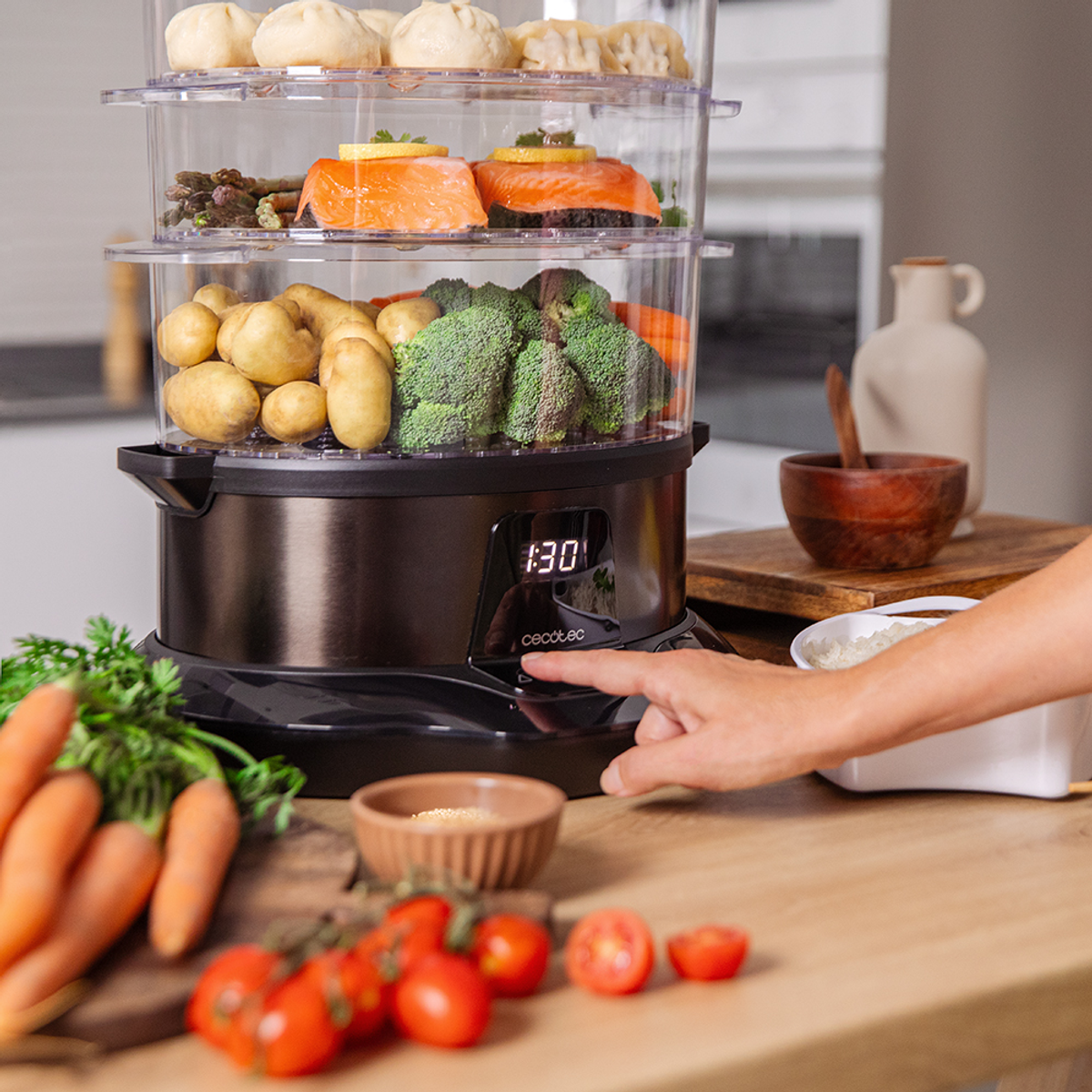 Una vaporiera con cibo: salmone, patate, broccoli. Una mano preme un pulsante. Carote e pomodori in primo piano.