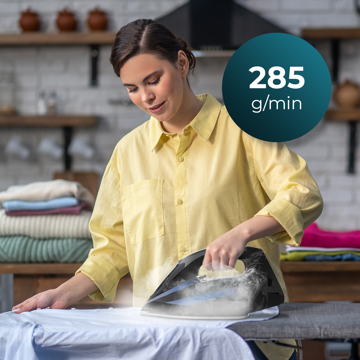 Una donna con una camicia gialla stira una camicia bianca. Il vapore sale dal ferro. Un cerchio blu mostra 285 g/min.