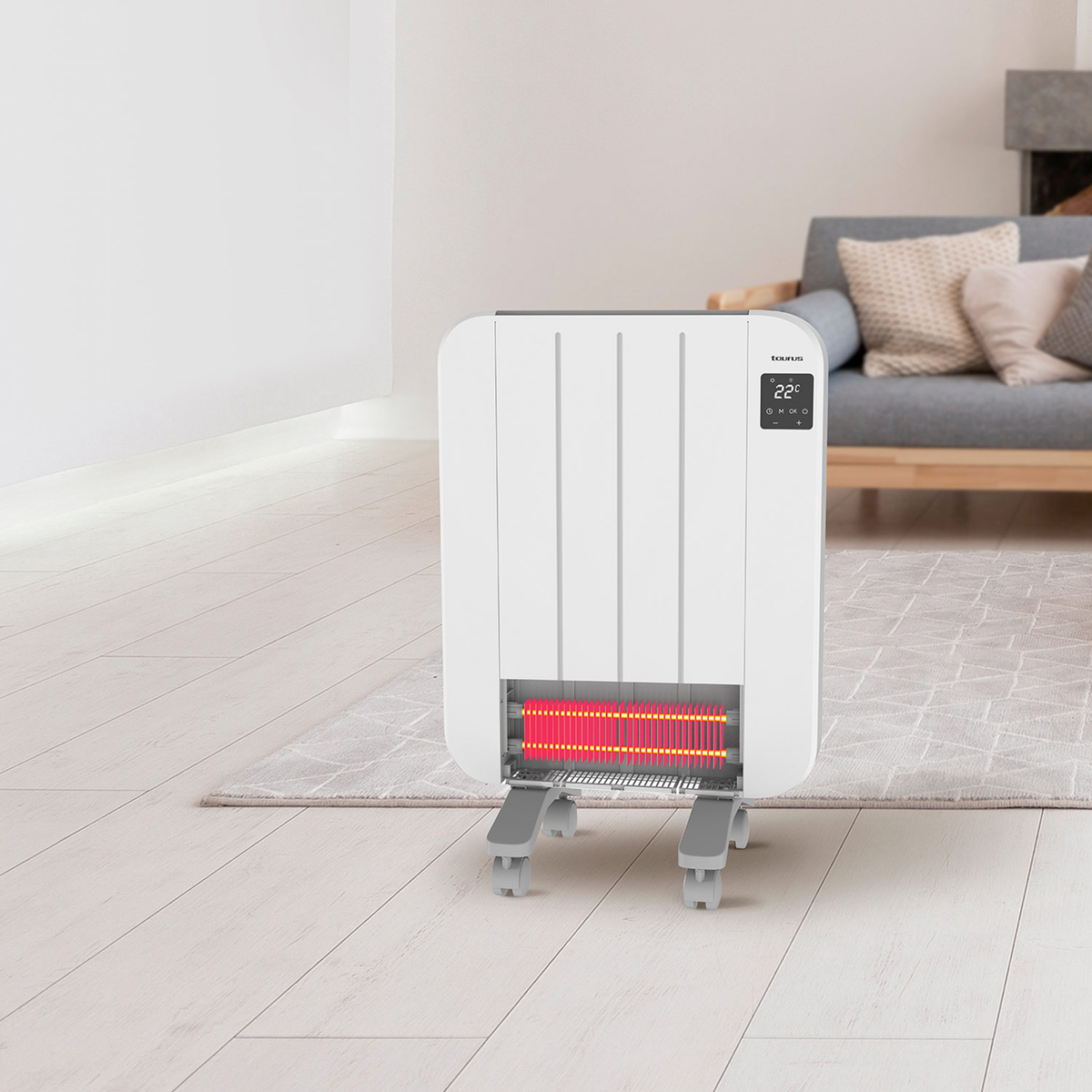 Un riscaldatore elettrico bianco è su un pavimento in legno chiaro. Il riscaldatore ha un display digitale ed è di fronte a un divano grigio.