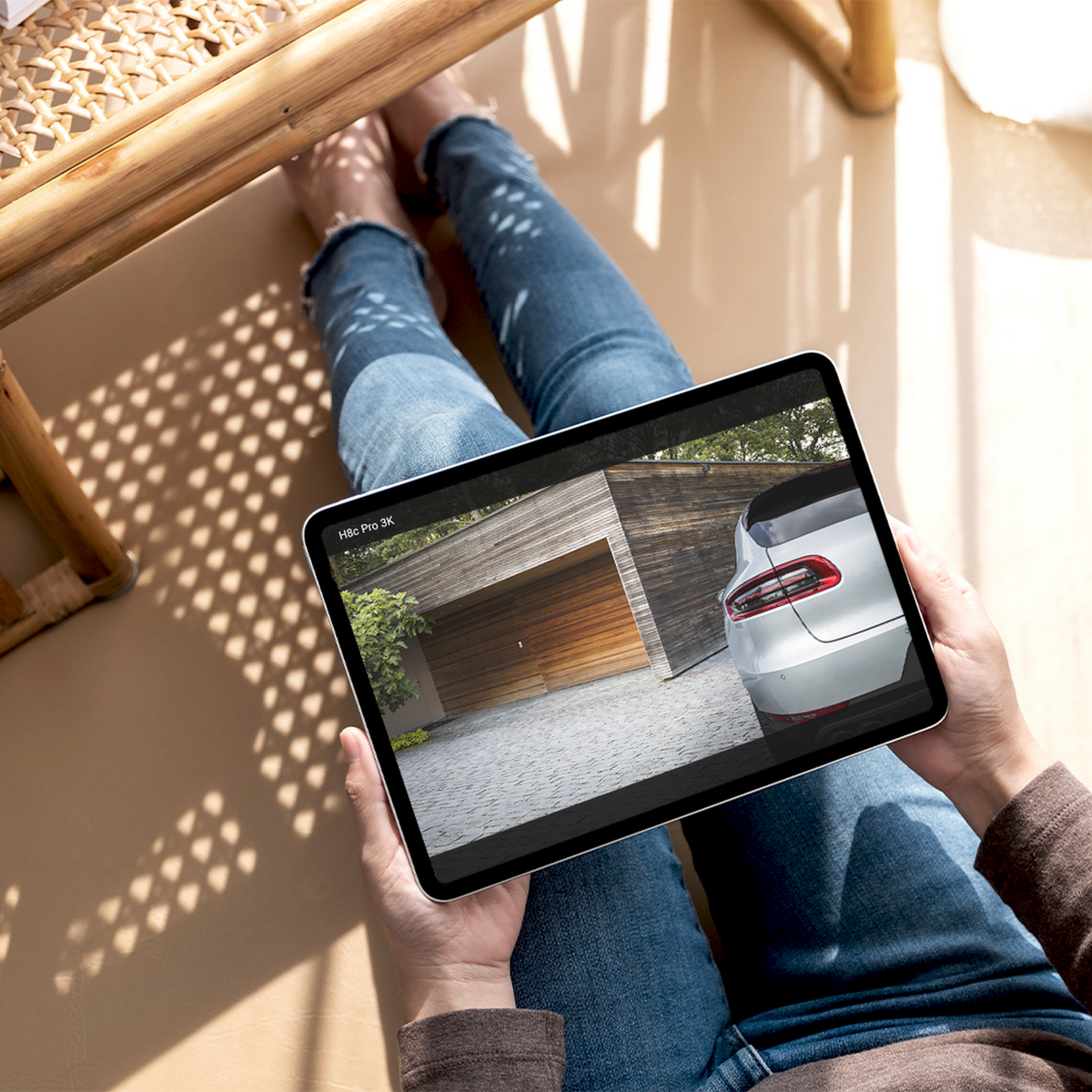 Osoba trzymająca tablet z nowoczesnym garażem i samochodem. Siedzą na podłodze w dżinsach. Cień krzesła.