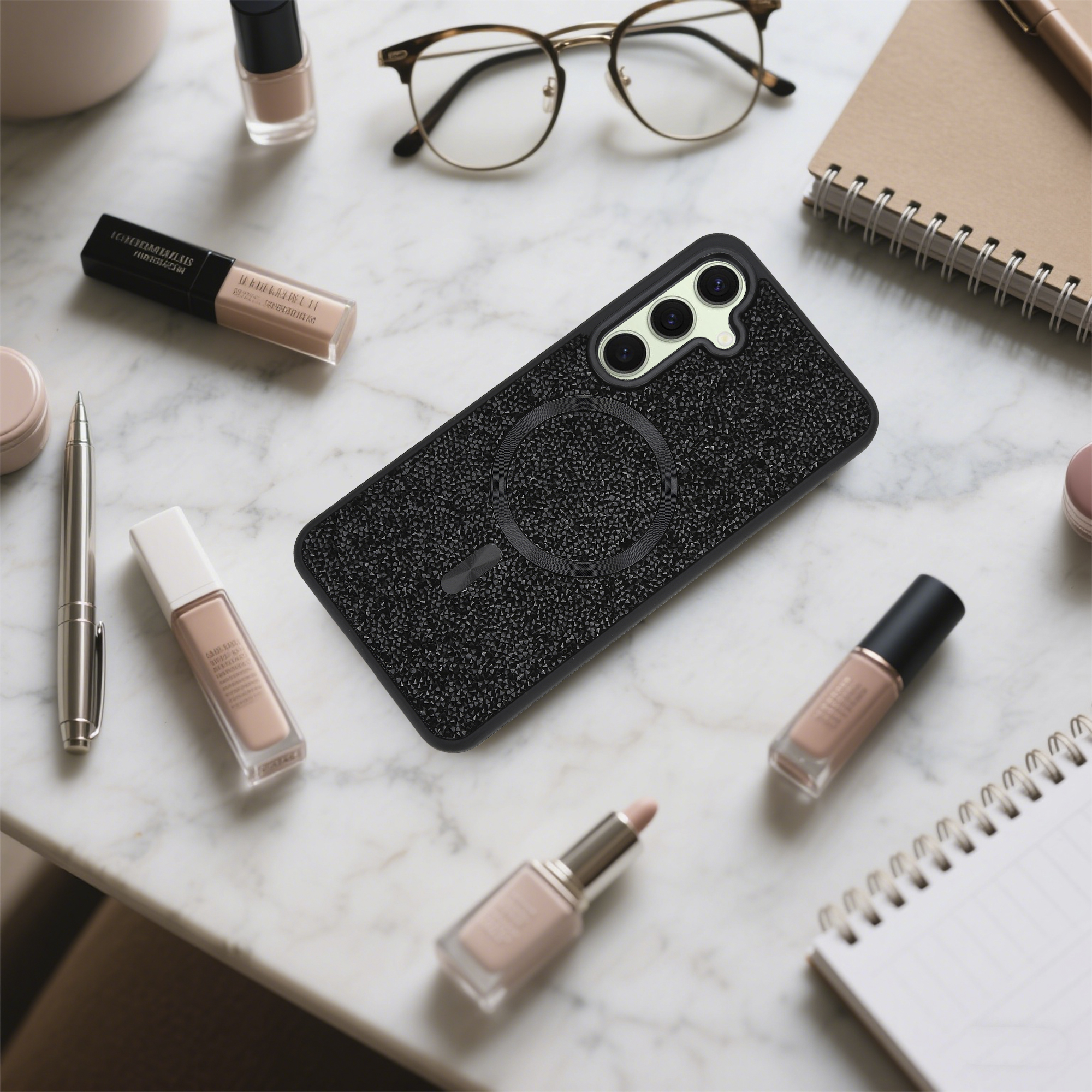 Auf einer Marmoroberfläche befinden sich eine Handyhülle und Make-up-Artikel. Im Hintergrund befinden sich eine Brille und ein Notizbuch.